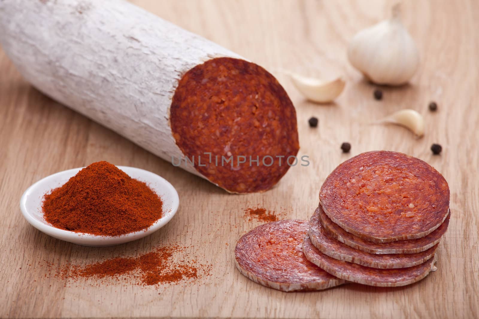 Traditional Hungarian speciality sliced sausage salami on wooden board with garlic, corns of black pepper and bowl with milled paprika spice