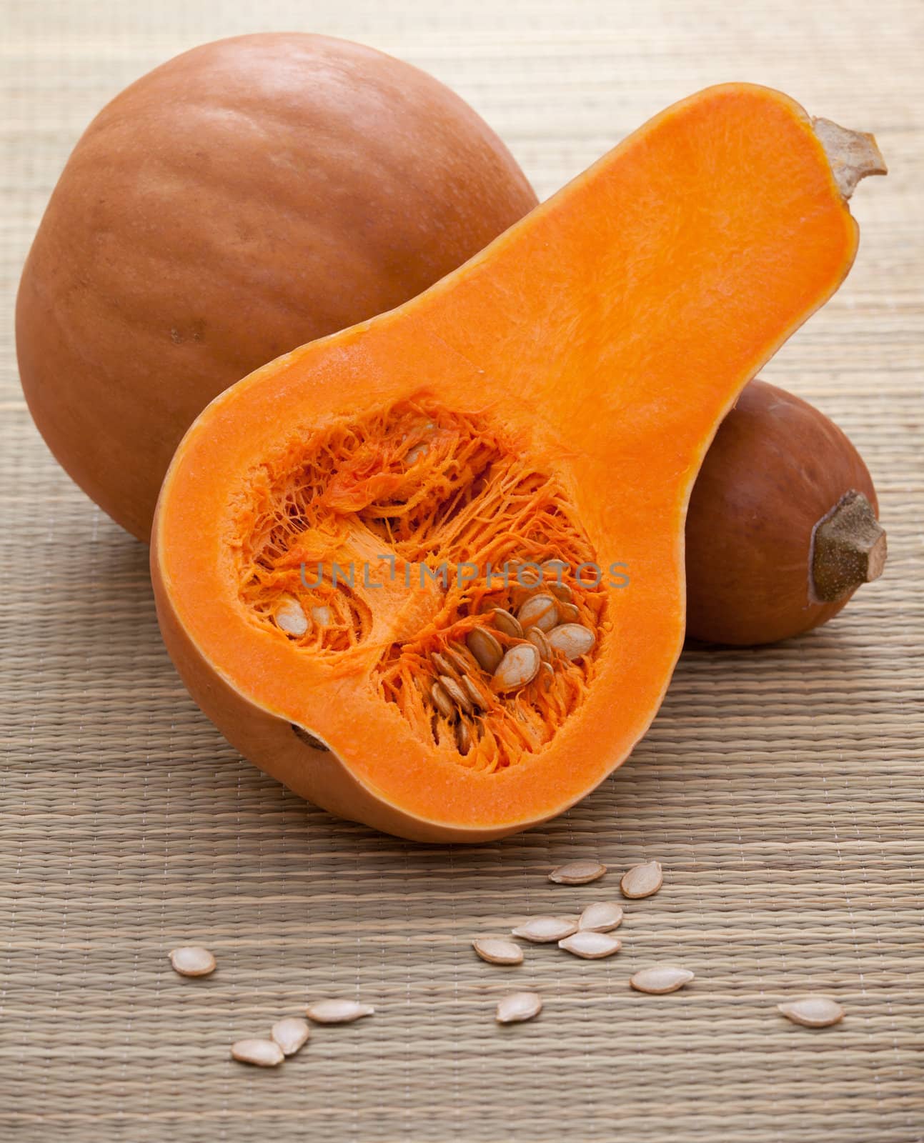 Ripe orange gourds and half with white seeds on rural straw woven surface and stripy background