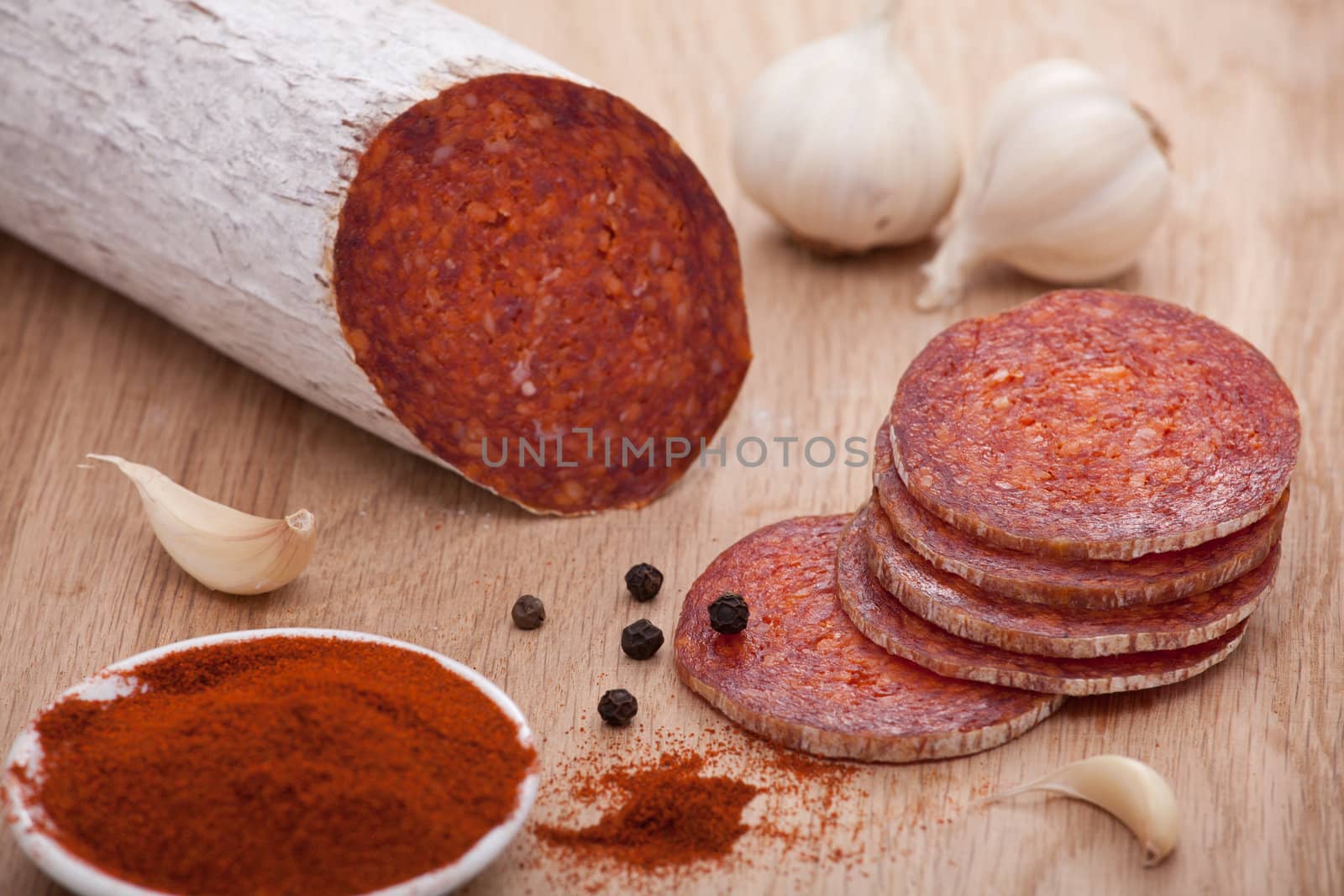 Traditional Hungarian speciality sliced sausage salami on wooden board with garlic, corns of black pepper and bowl with milled paprika spice