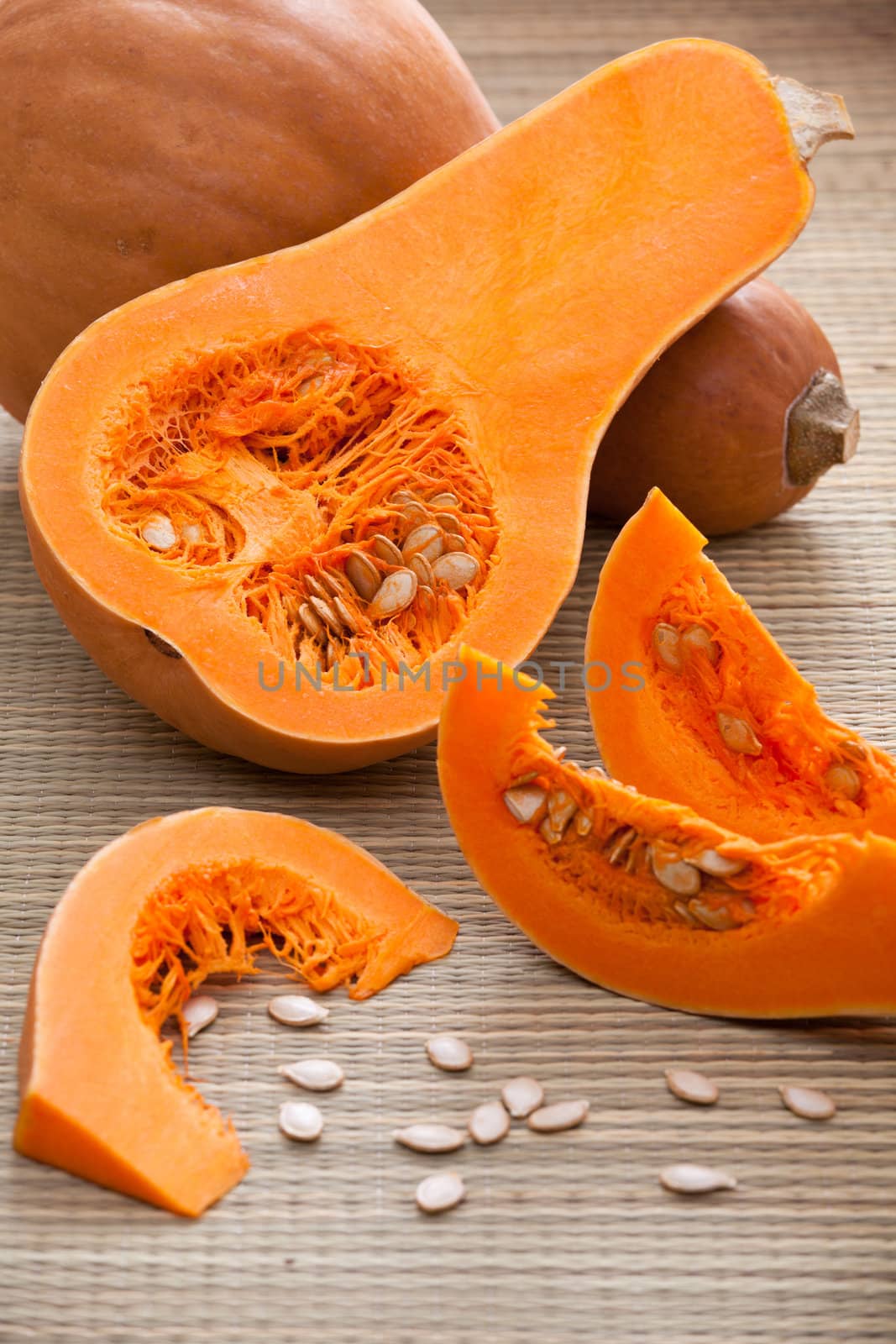 Ripe orange gourds and half, sliced fleshy segments and white seeds on rural straw woven surface and stripy background