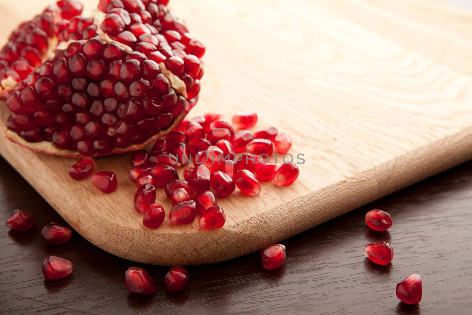 Pomegranate slices and handful of seeds on wooden background with empty place for text