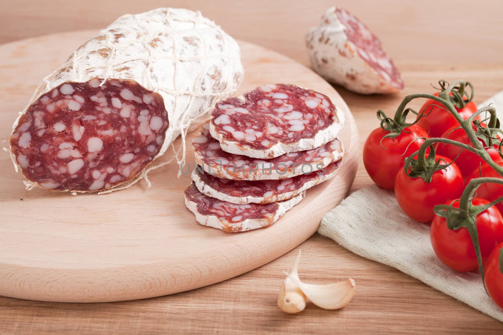 Traditional sliced salami on wooden board with garlic, cherry tomatoes