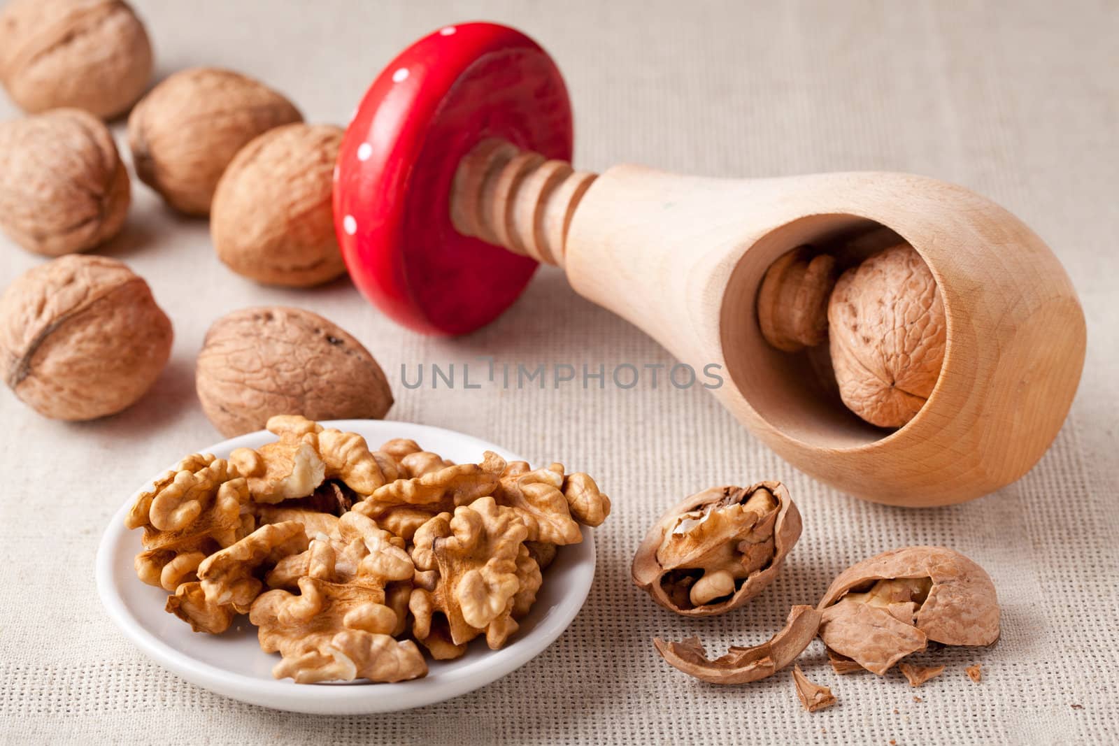 Cores of matured nuts in plate, brown Circassian walnuts,  nutshell and wooden handmade nutcracker like fungus amanita on the linen tablecloth