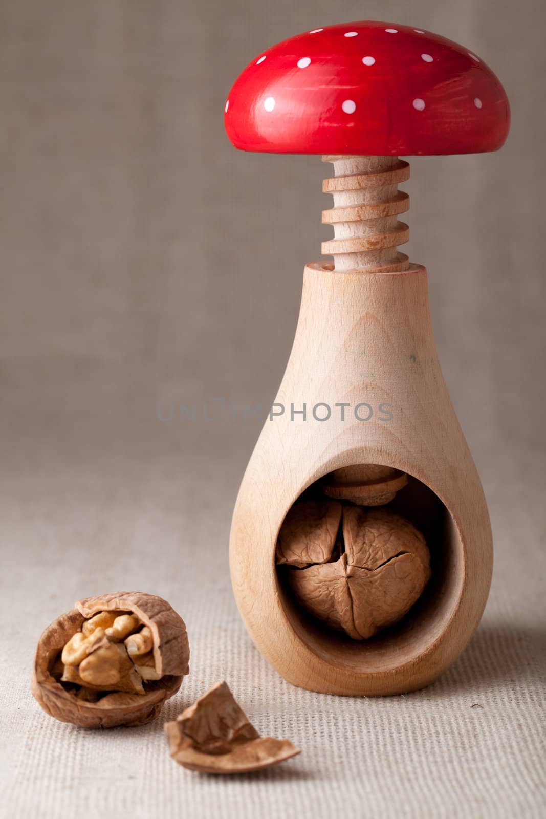 Cracked brown Circassian walnuts, nut core, shell, wooden handmade nutcracker like fungus amanita on linen tablecloth background