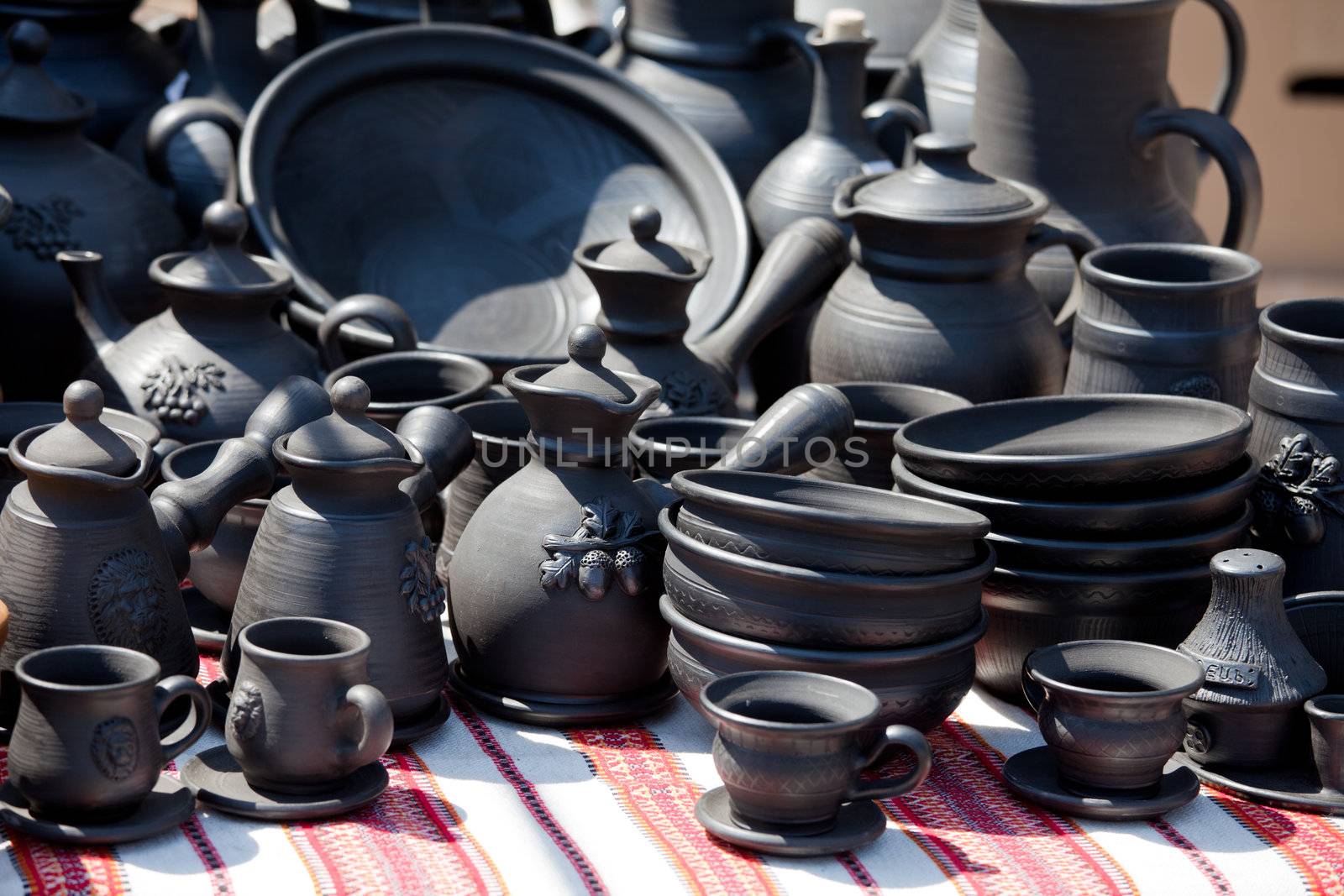 Rustic handmade black ceramic pottery souvenirs (plates, bowls, teapots, cups) on embroidered traditional Ukrainian towel at street handicraft market