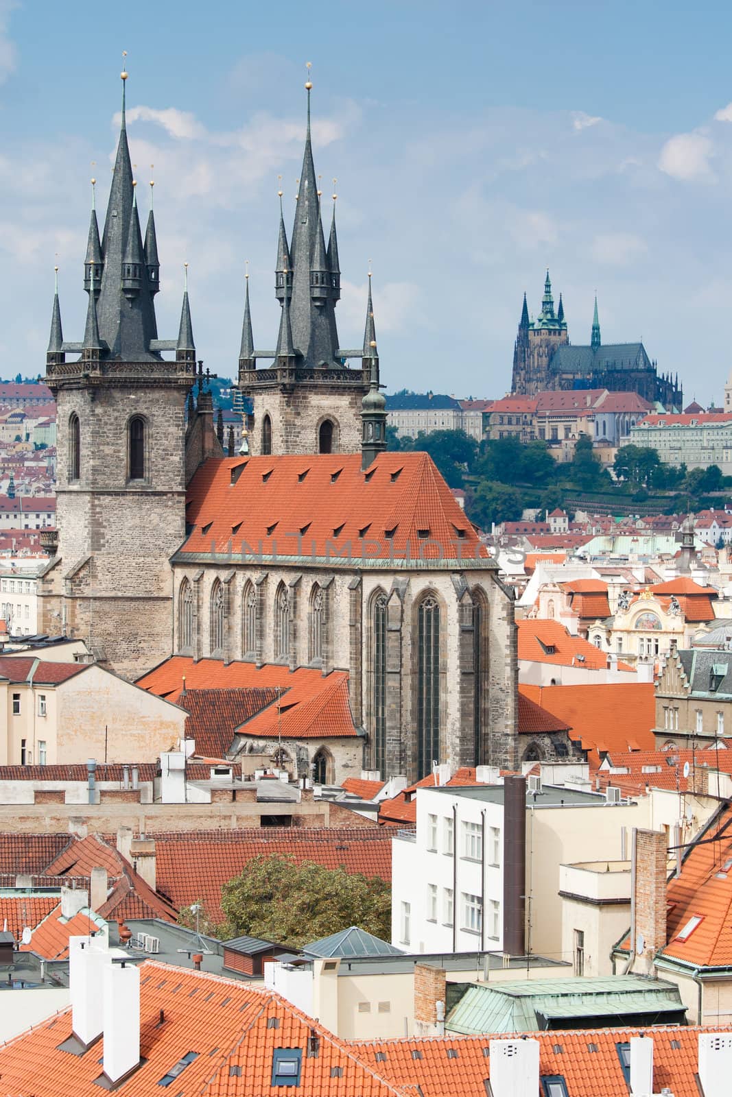 Top view cityscape on red tiled mansard roofs, old district, Gothic cathedral of Virgin Mary before Tyn and Prague castle on blue sky background