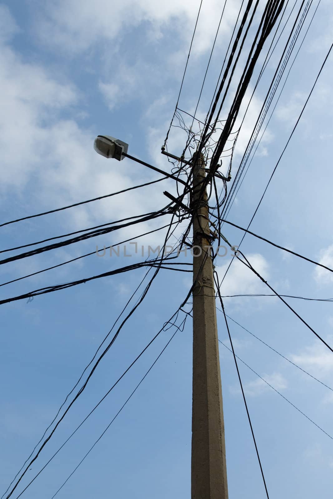 Lamp pole and tangled electric wires on the blue sky background. Vertical