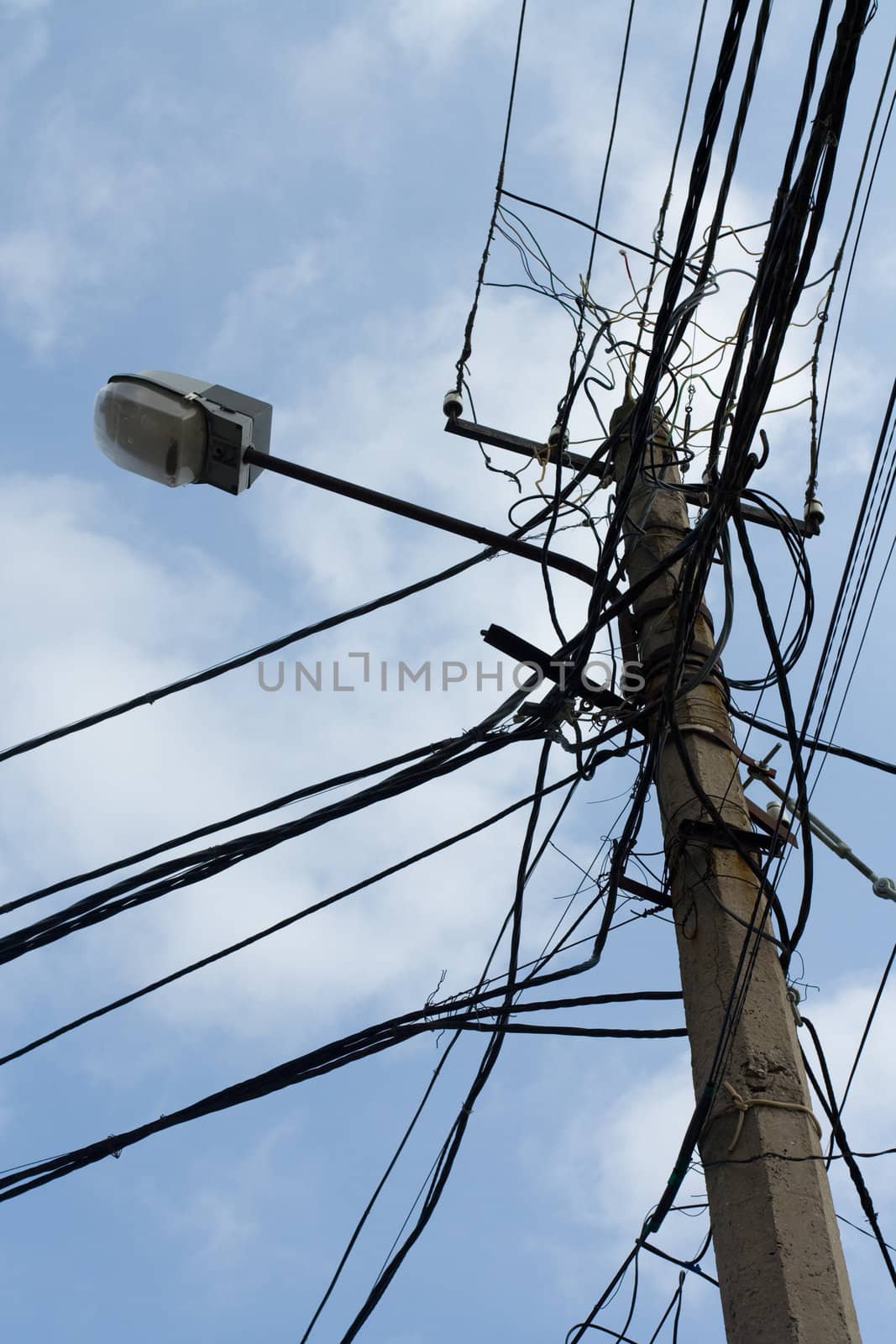 Lamp pole and tangled electric wires on the blue sky background. Vertical