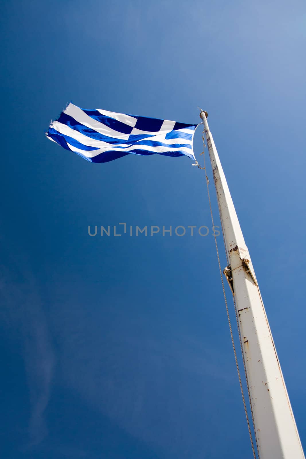 Flying Greek Flag hoisted on flagpole on the blue sky background