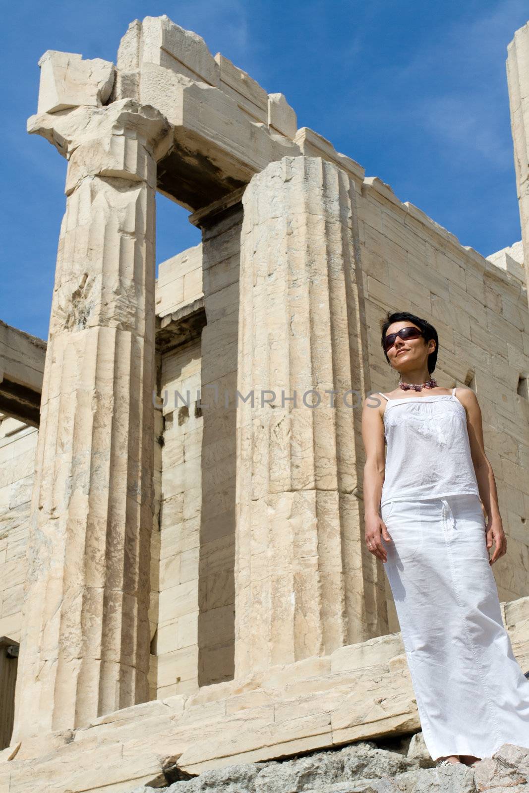 Close-up young woman dressed white near the columns of entrance propylaea to ancient temple Parthenon in Acropolis Athens Greece on blue sky background