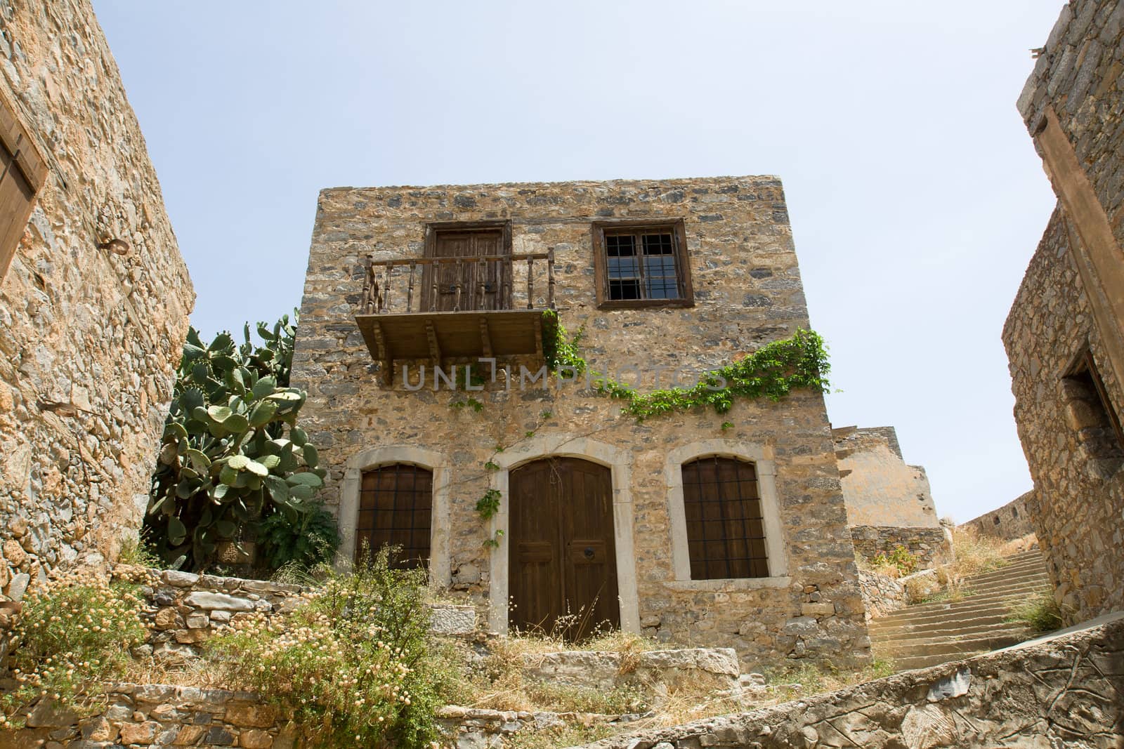 Picturesque old Mediterranean style abandoned lopsided rustic stone house with wooden sun blind, balcony in ancient town