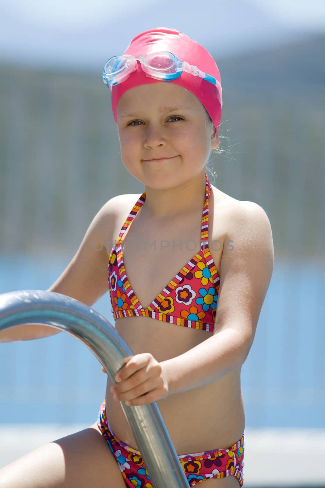 Close-up portrait of smiling cute little child in bathing cap, glasses near swimming pool stairs