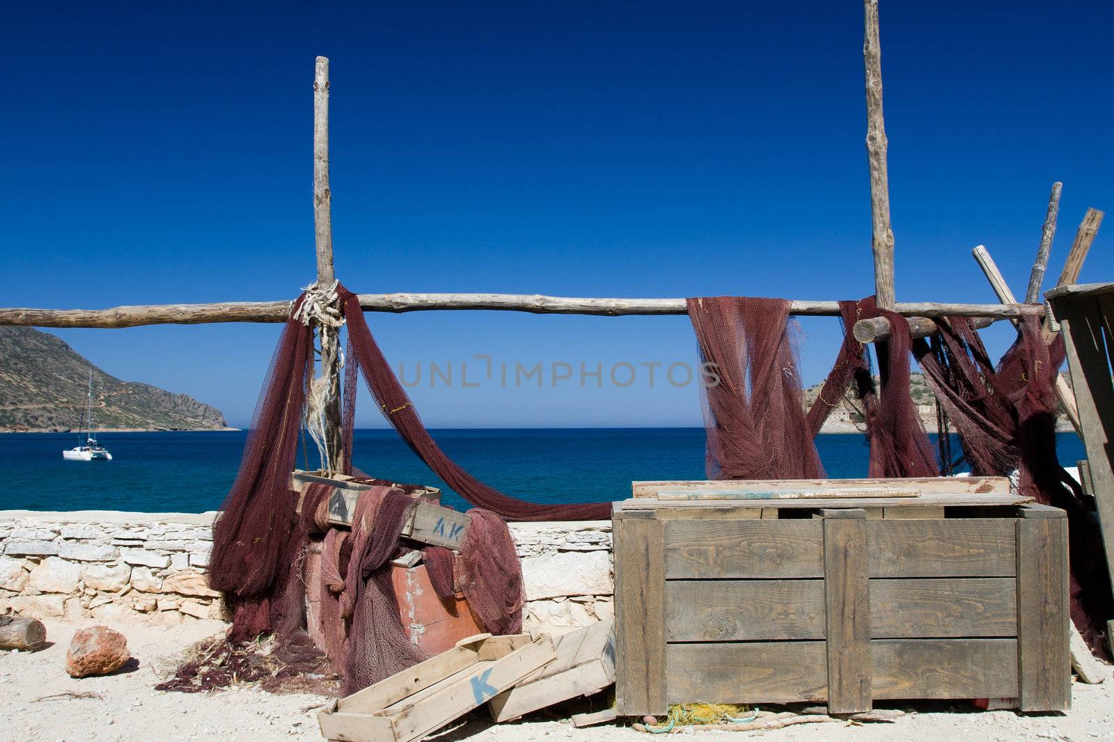 Picturesque marine landscape: drying fishing net, wooden chest on the background of blue sea, sky and mountain