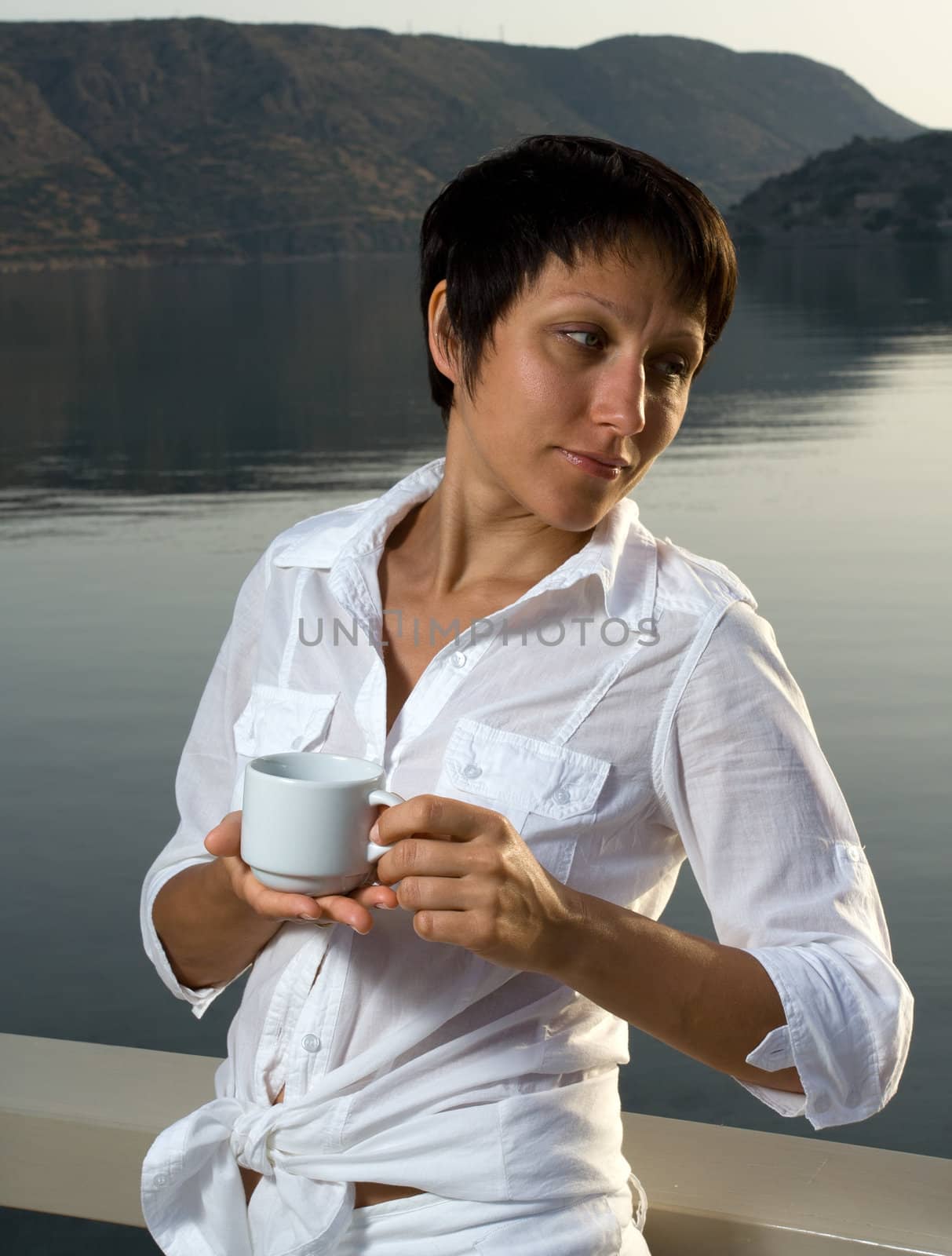 Young dressed white brunette woman meets sunrise drinking morning coffee on the mountain and sea background