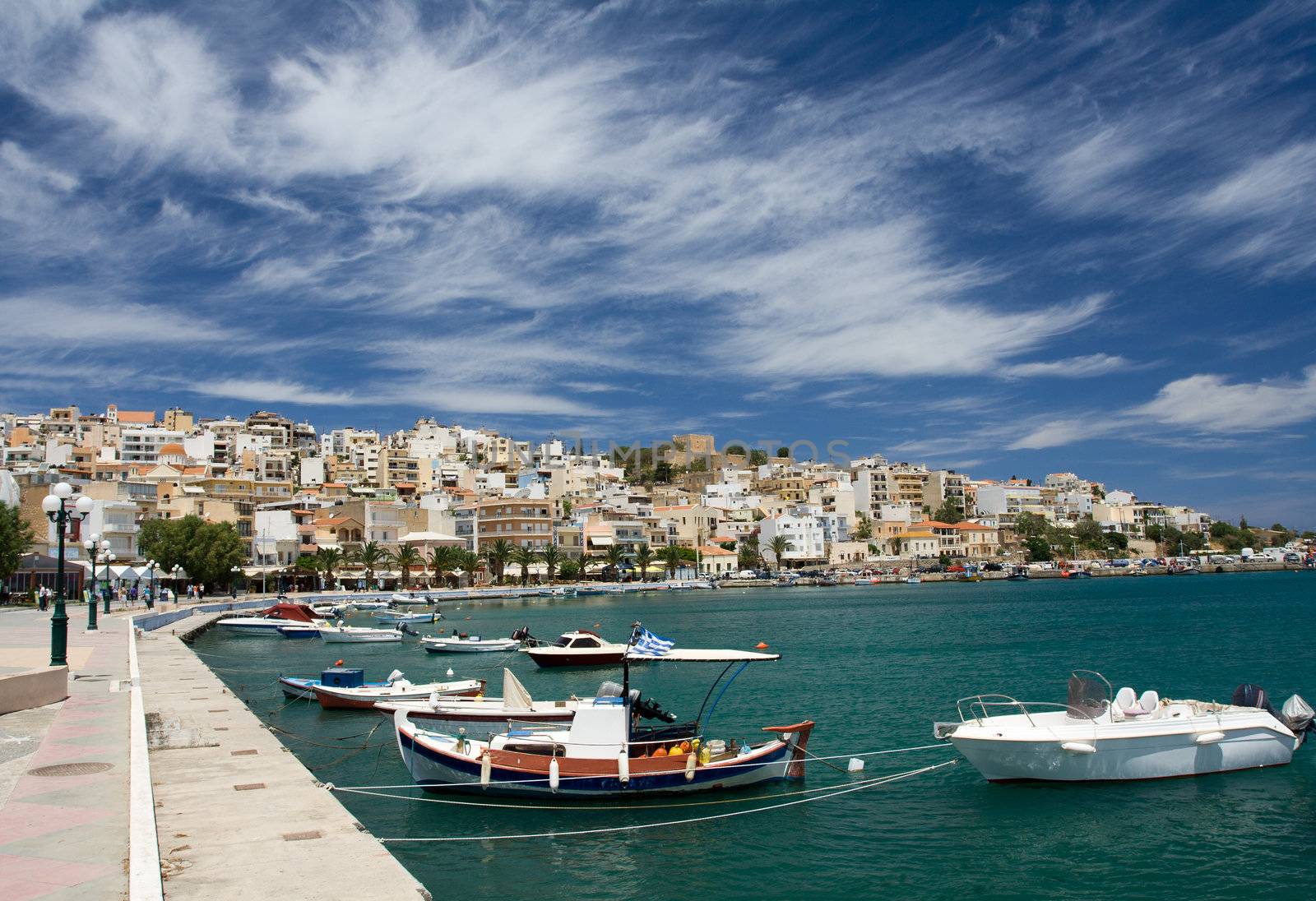 Sea bay with moored boats, promenade in Mediterranean town Sitia Greece Crete and dramatic cirrus clouds in the blue sky