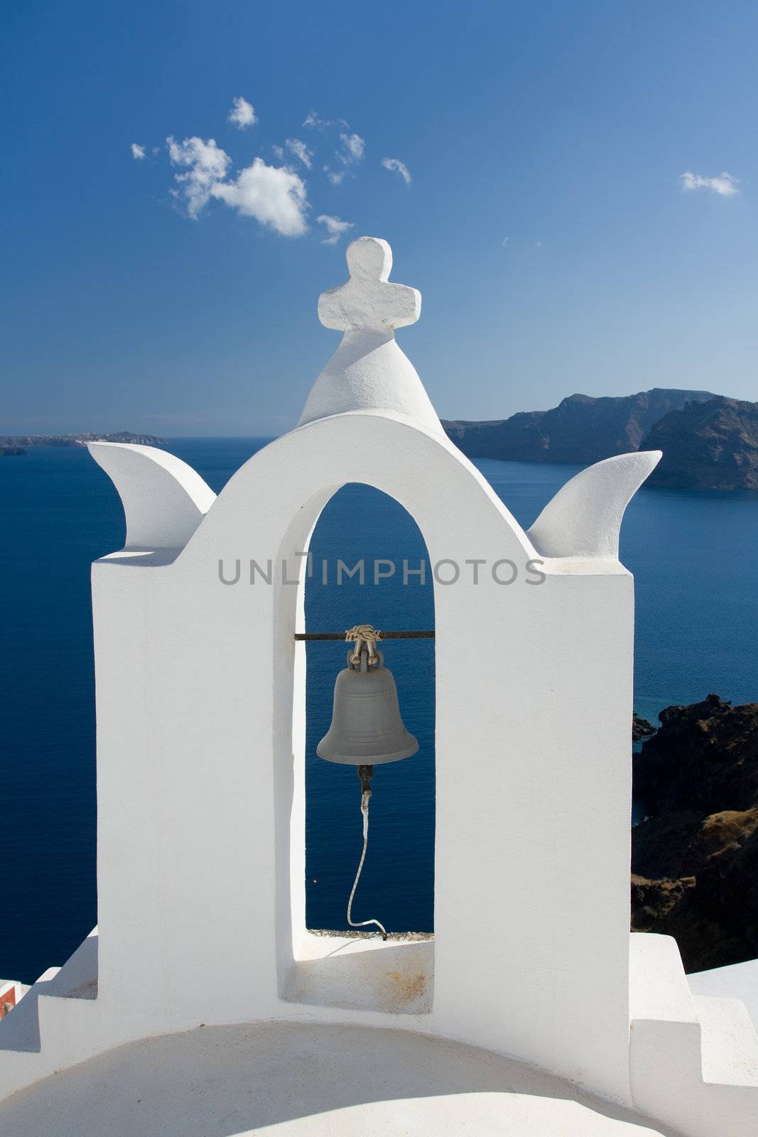 See view and cloudy sky through traditional white church arch and bell in village Oia of Cyclades Island Santorini Greece
