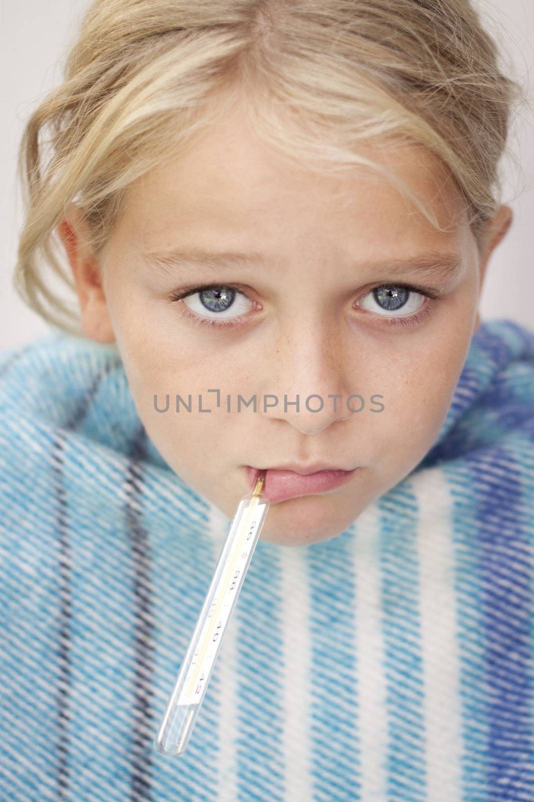 Child with a fever thermometer in her mouth, looking sad and sick