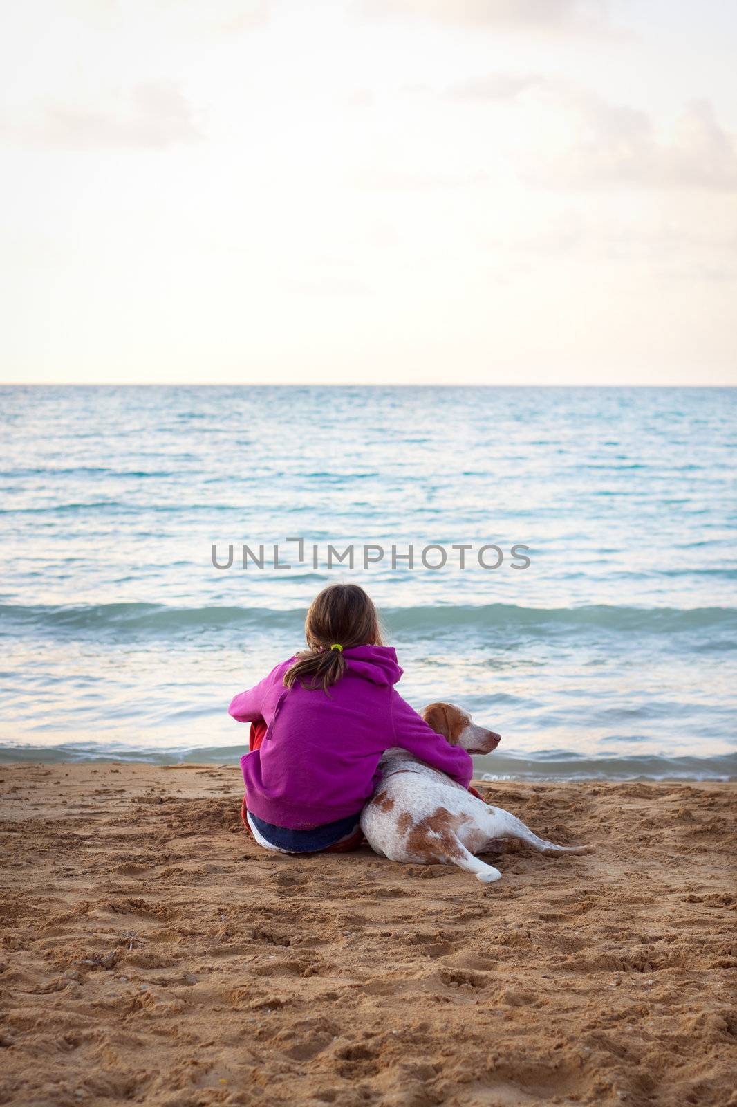 A young female looking out at sea, cuddling her pet dog. Slight vignette