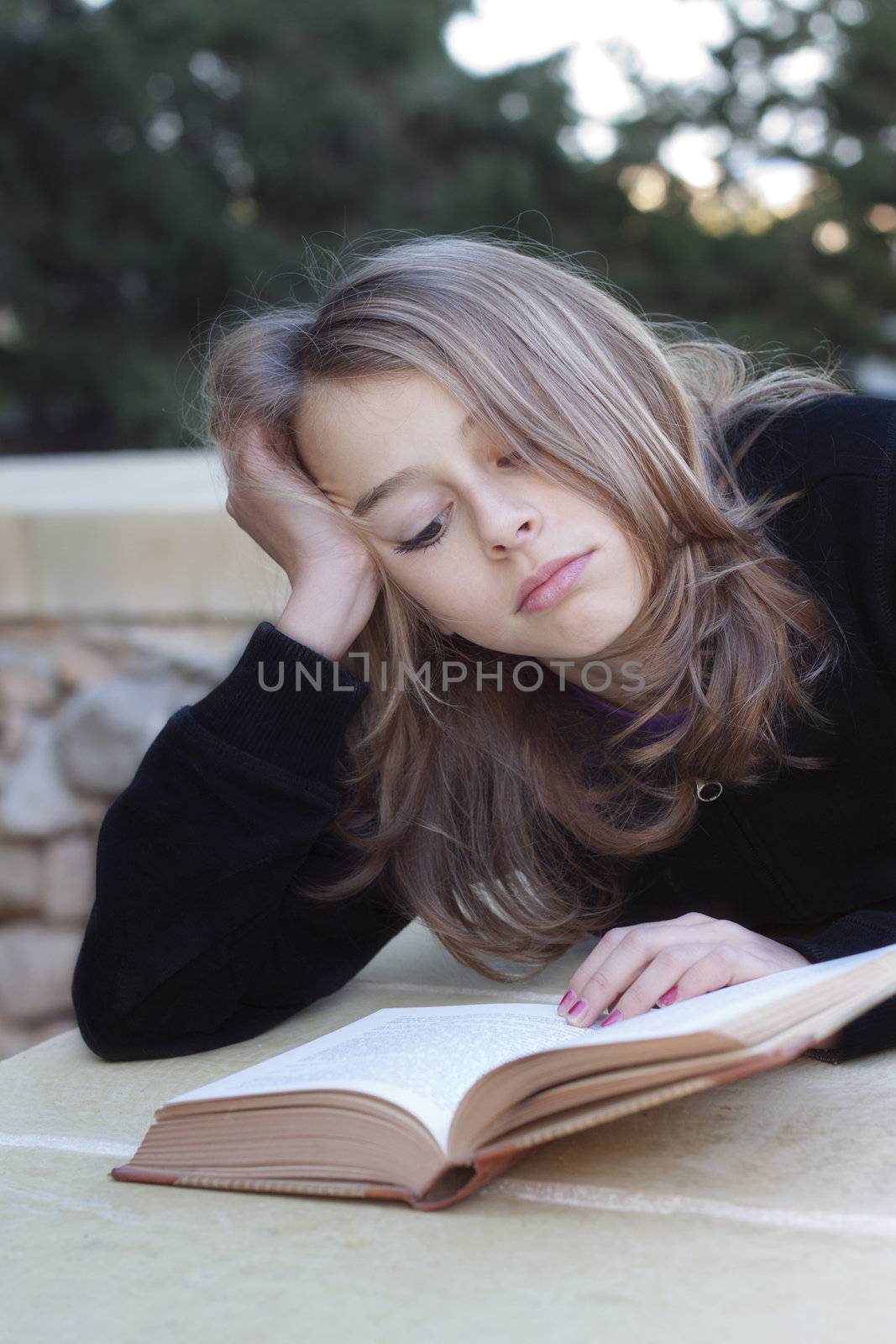 A sulky teenager lying down reading a book, not happy, having problems