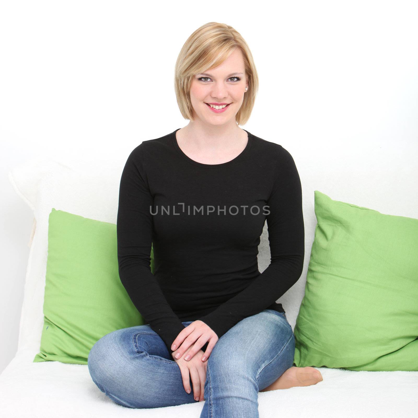 Pretty relaxed woman sitting on a couch with her bare foot tucked up under her wearing jeans and a casual black top