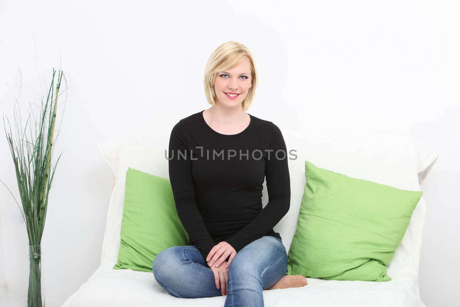 Casual sexy young lady relaxing on a sofa in her living room in jeans and a casual black top with her bare foot tucked up under her