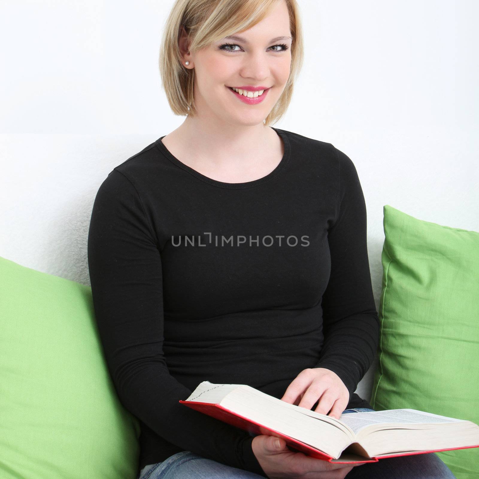 Closeup cropped portrait of a smiling woman sitting amongst comfortable cushions enjoying her book