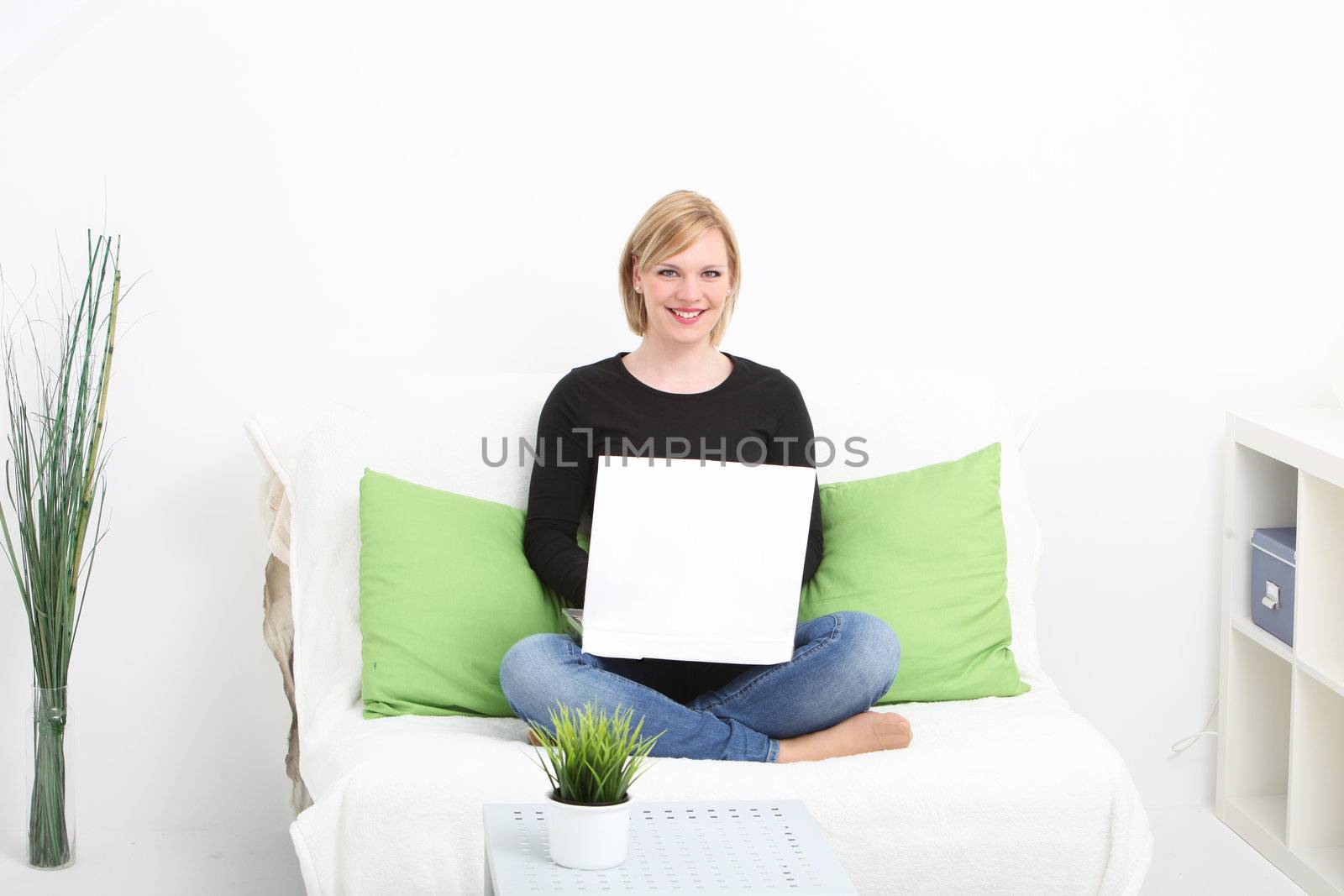 An attractive blonde woman sits on a sofa in a simple domestic setting, holding a blank, white card with space for your text