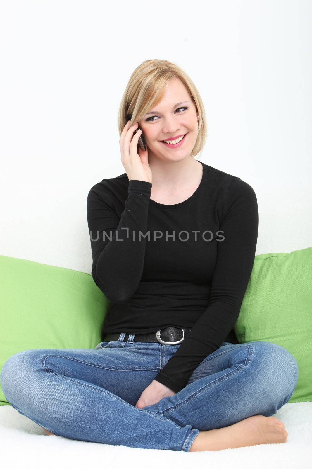 Smiling casual young woman chatting on her mobile sitting cross legged on a couch barefoot in jeans