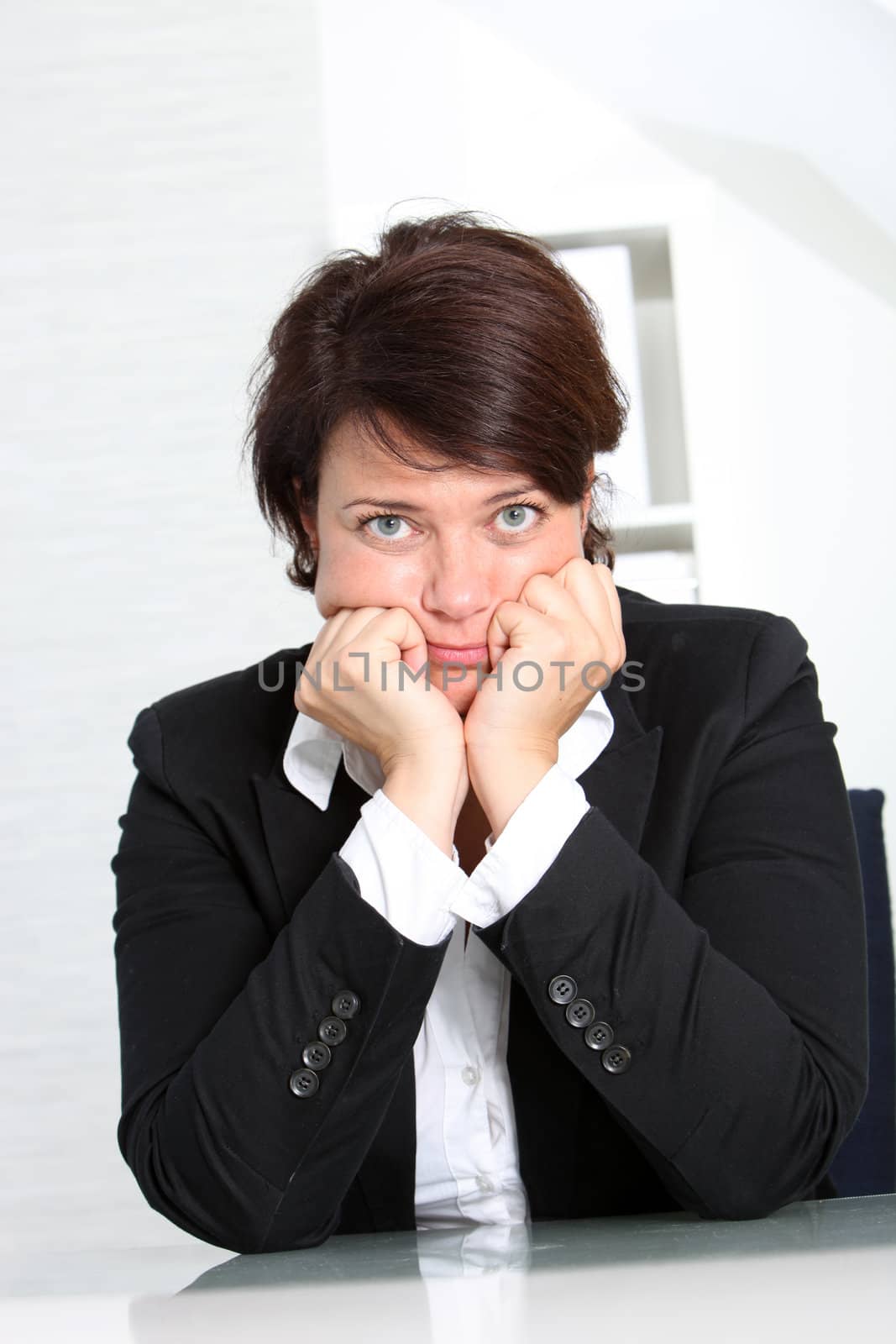 Dejected businesswoman seated at her desk with her chin on her hands looking gloomily at the camera
