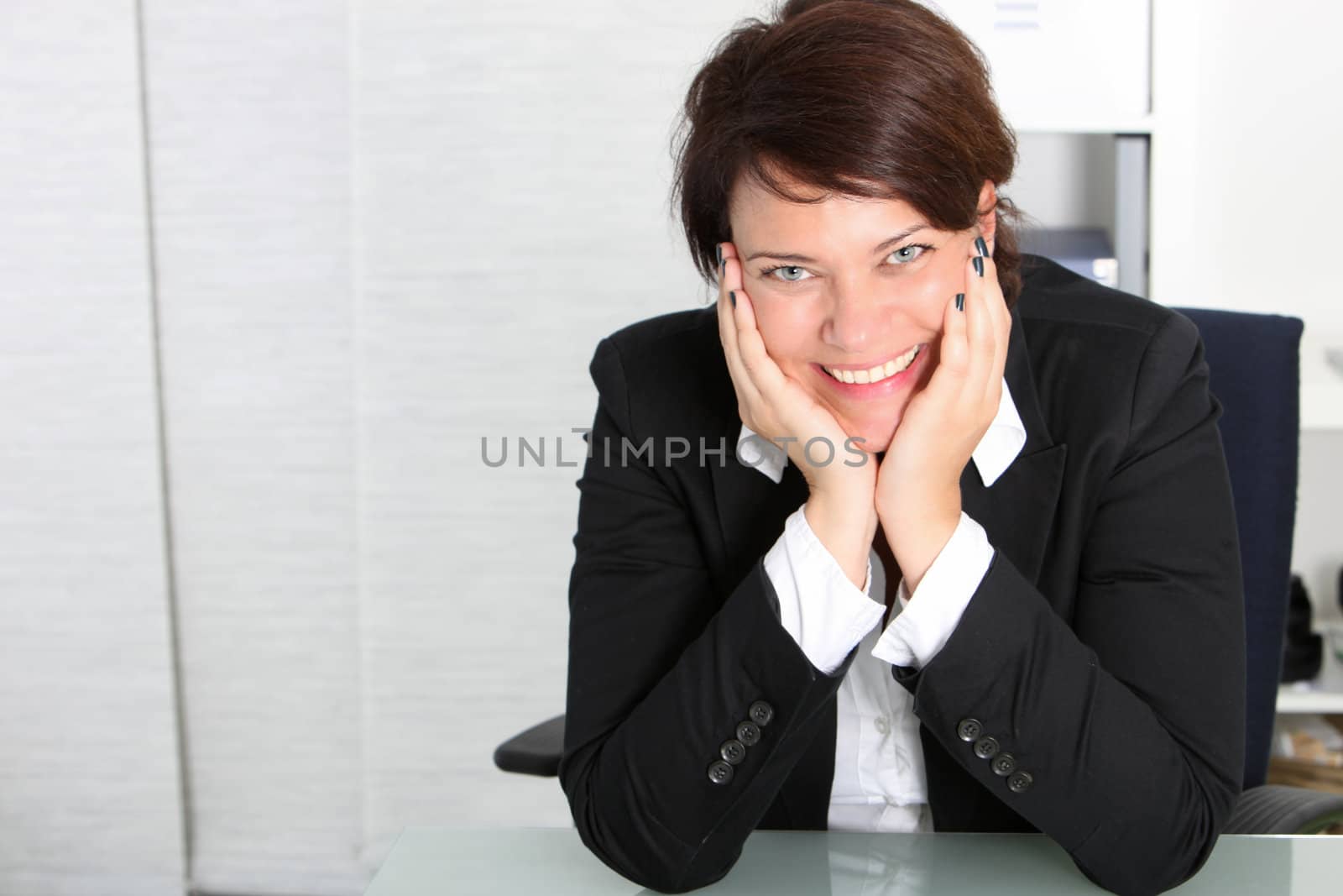 Smiling attractive business professional sitting at her desk with her chin resting in her cupped hands