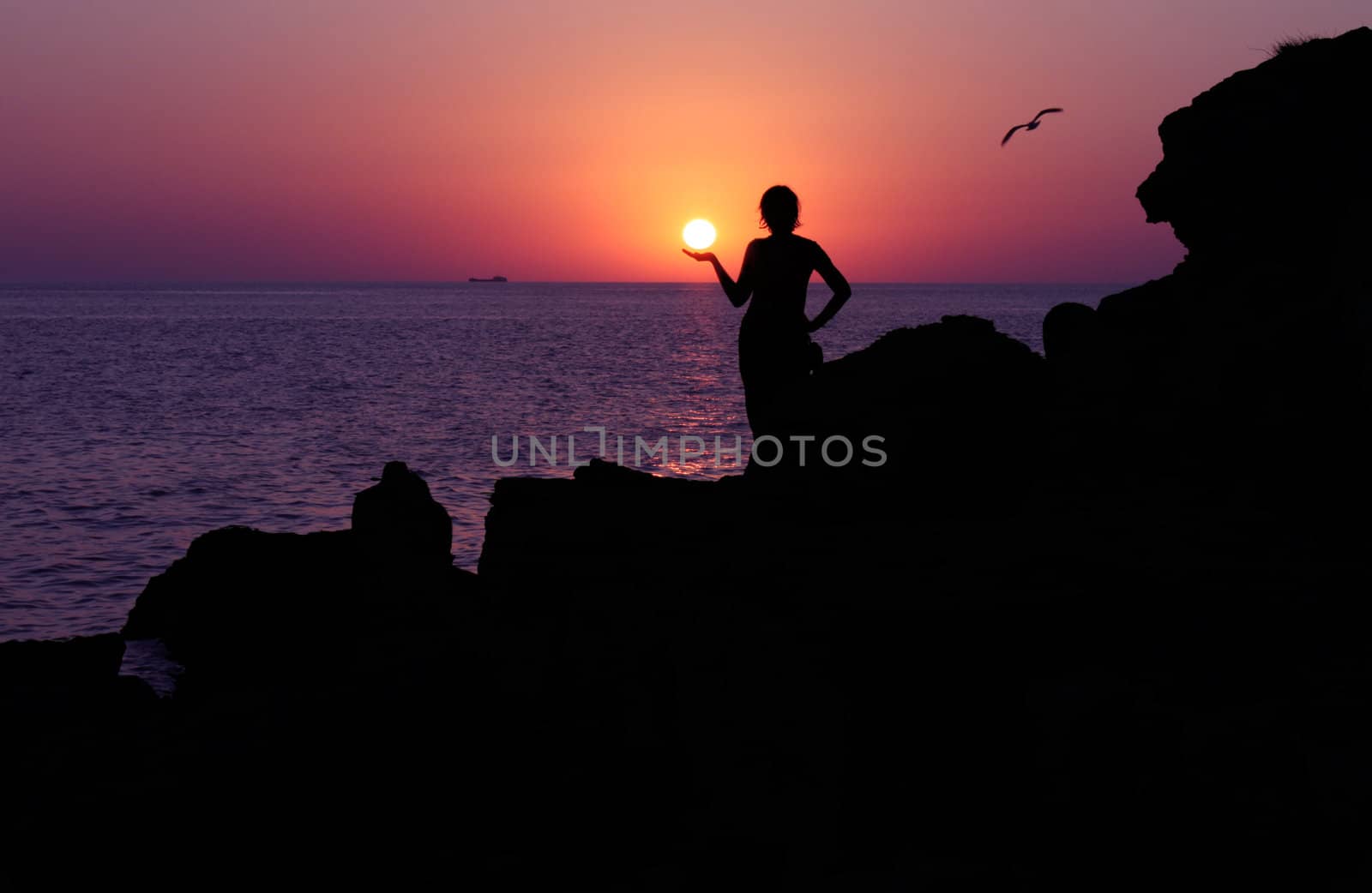 silhouette of girl holding sun at sunset near sea