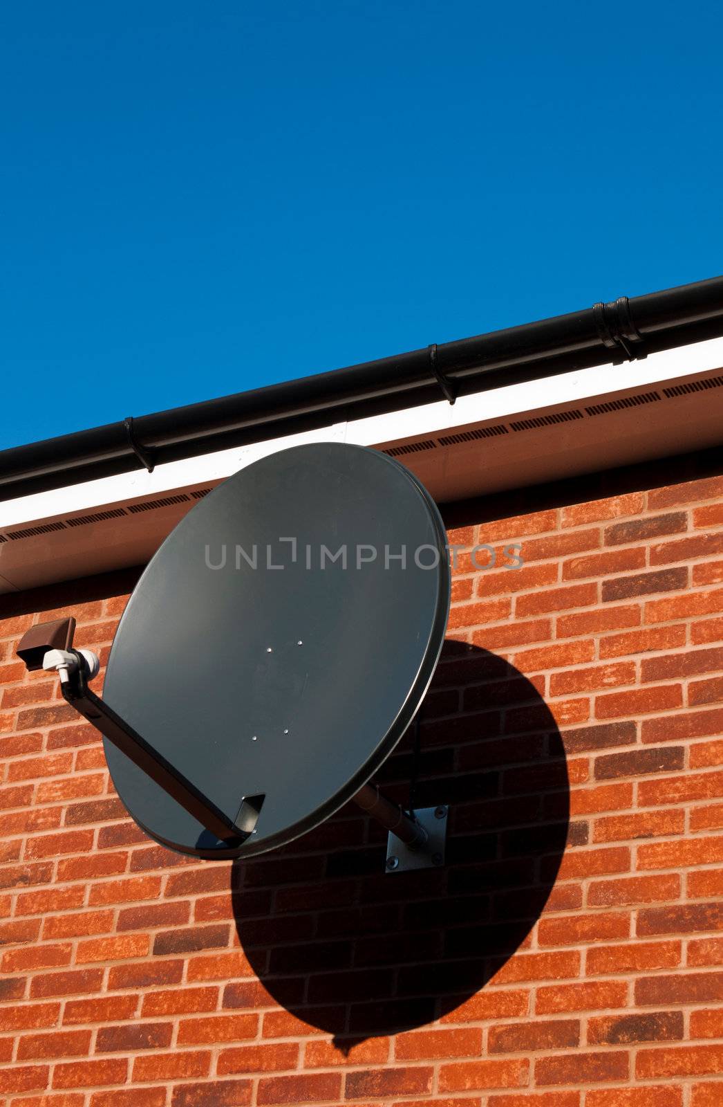 black satellite dish attached to brick wall (residential house, copy-space available)