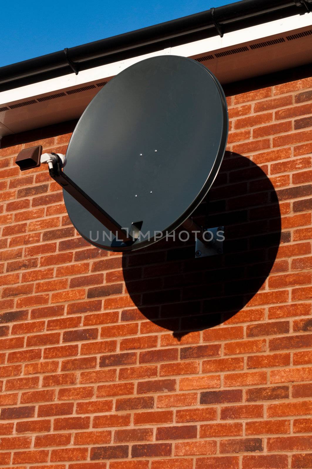 black satellite dish attached to brick wall (residential house, copy-space available)