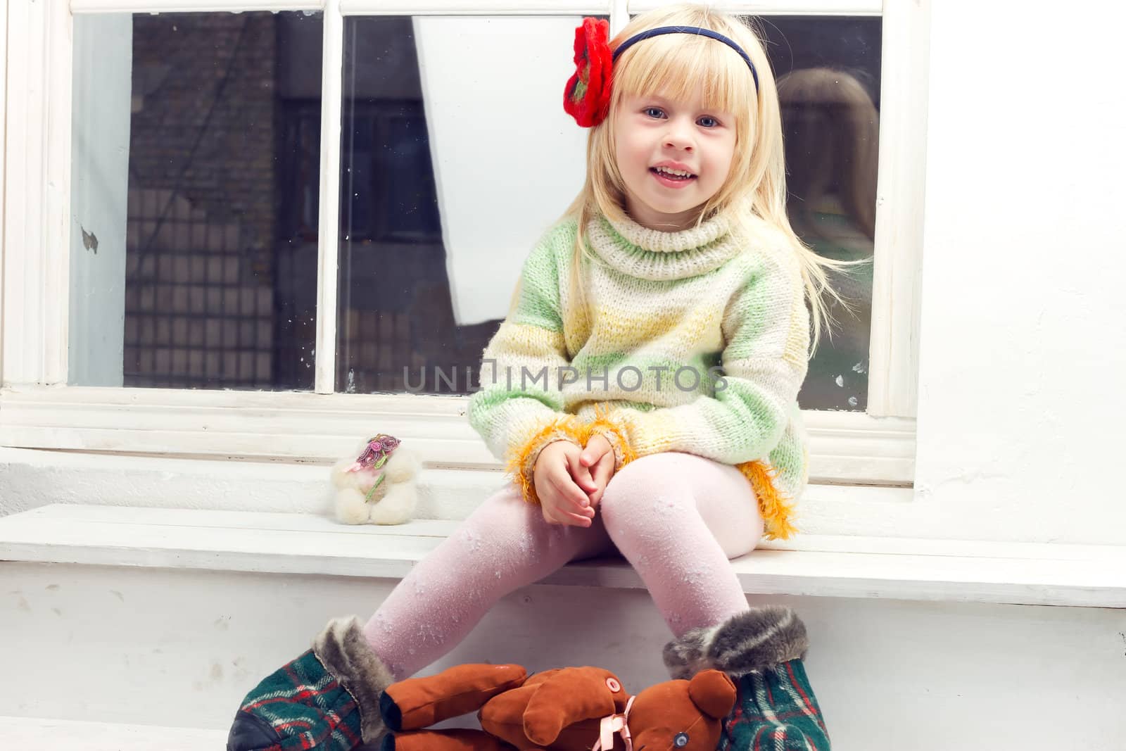 blonde little girl in knitted sweater sitting on the window