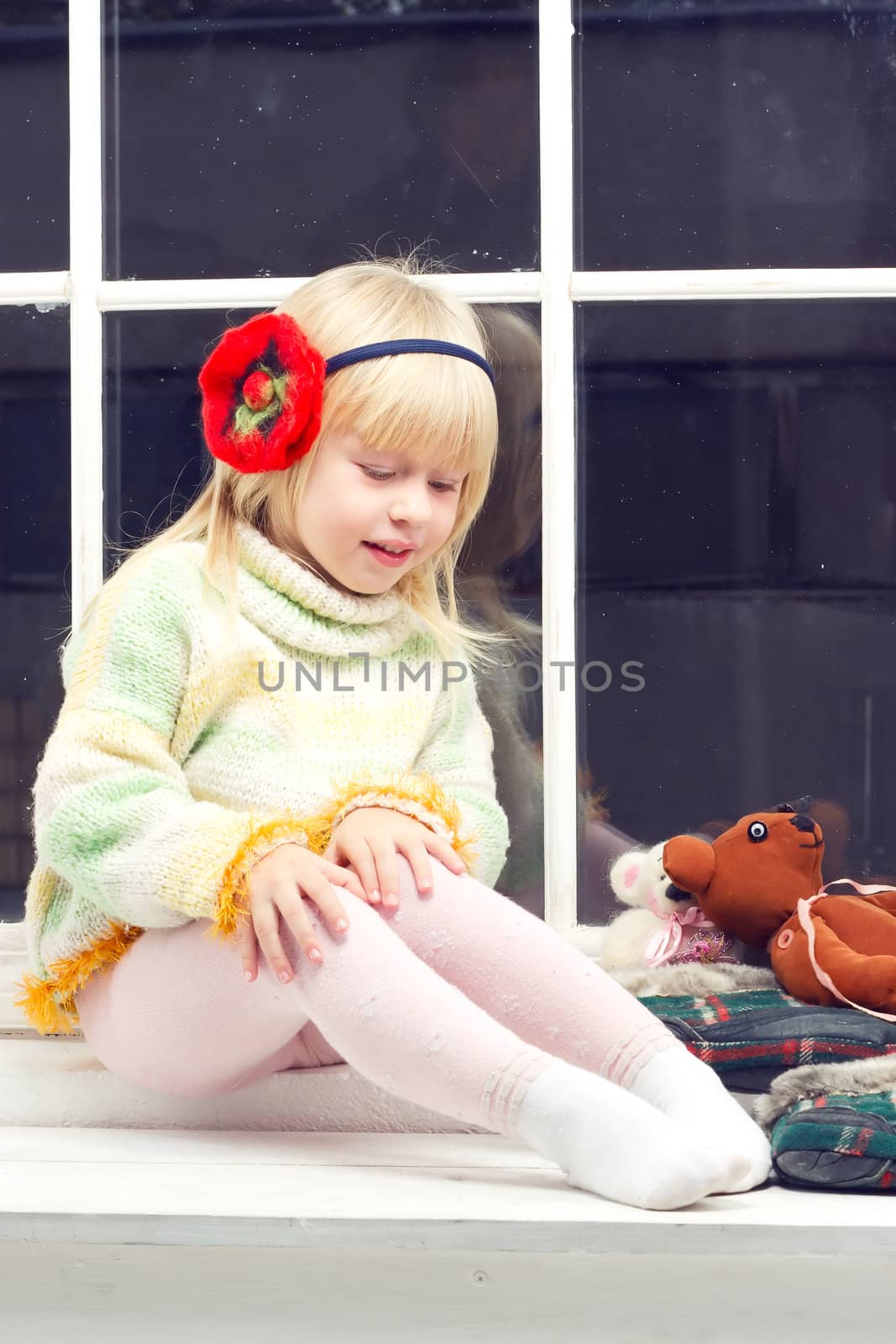 beautiful little girl blonde in a knit sweater sitting near the window of toys