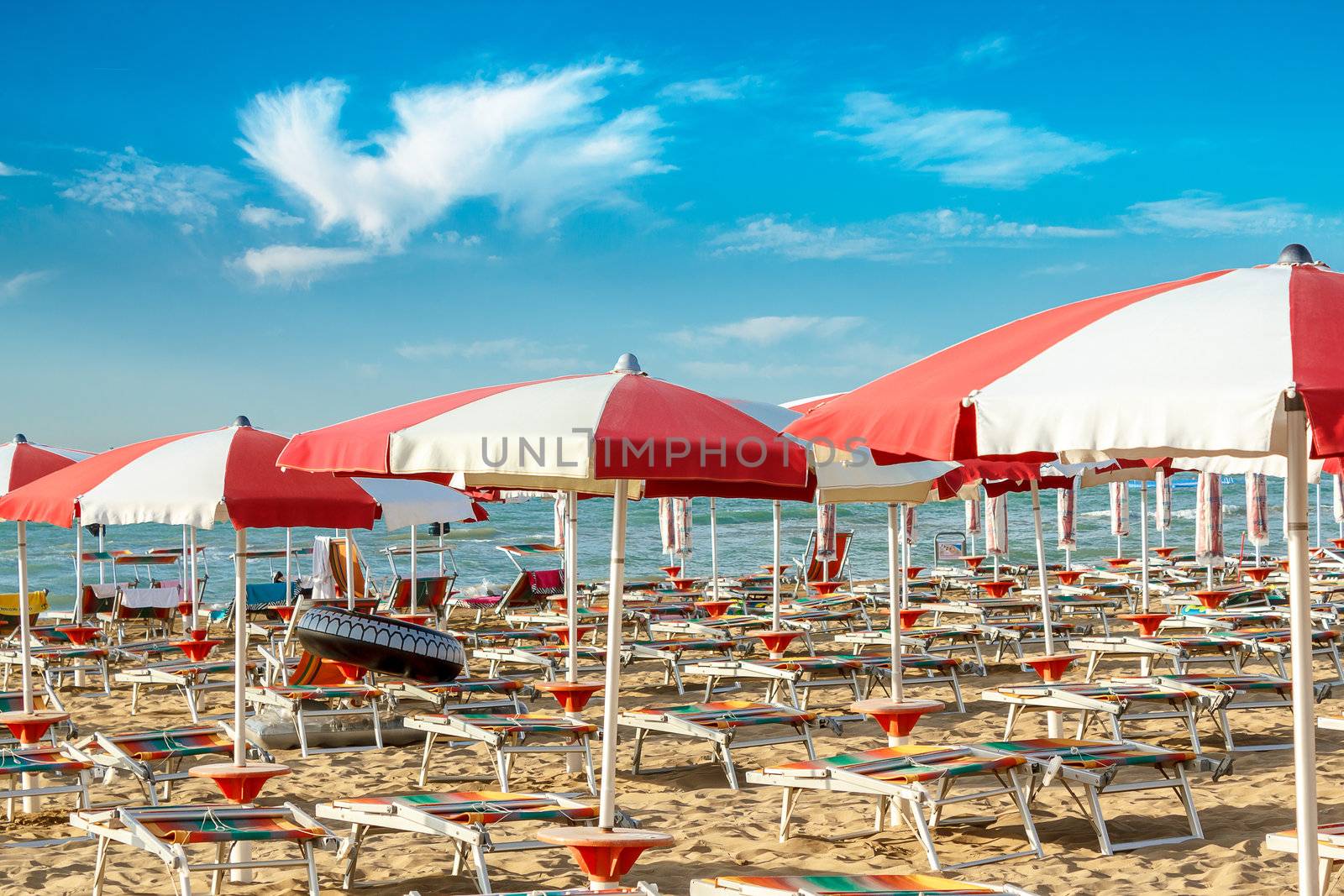 red and white umbrellas and sunlongers on the sandy beach in Italy