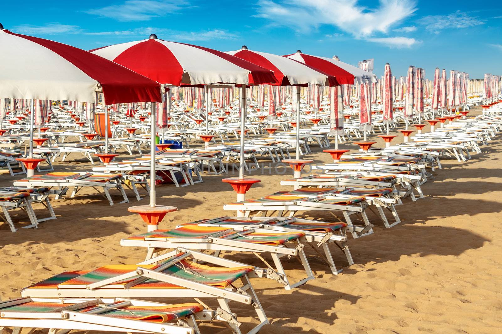 red and white umbrellas and sunlongers on the sandy beach in Italy