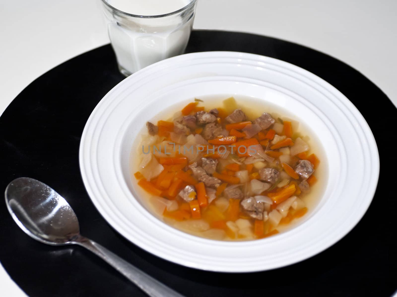 Close up of a lunchmeny consisting of a soup with meat and a glass of milk