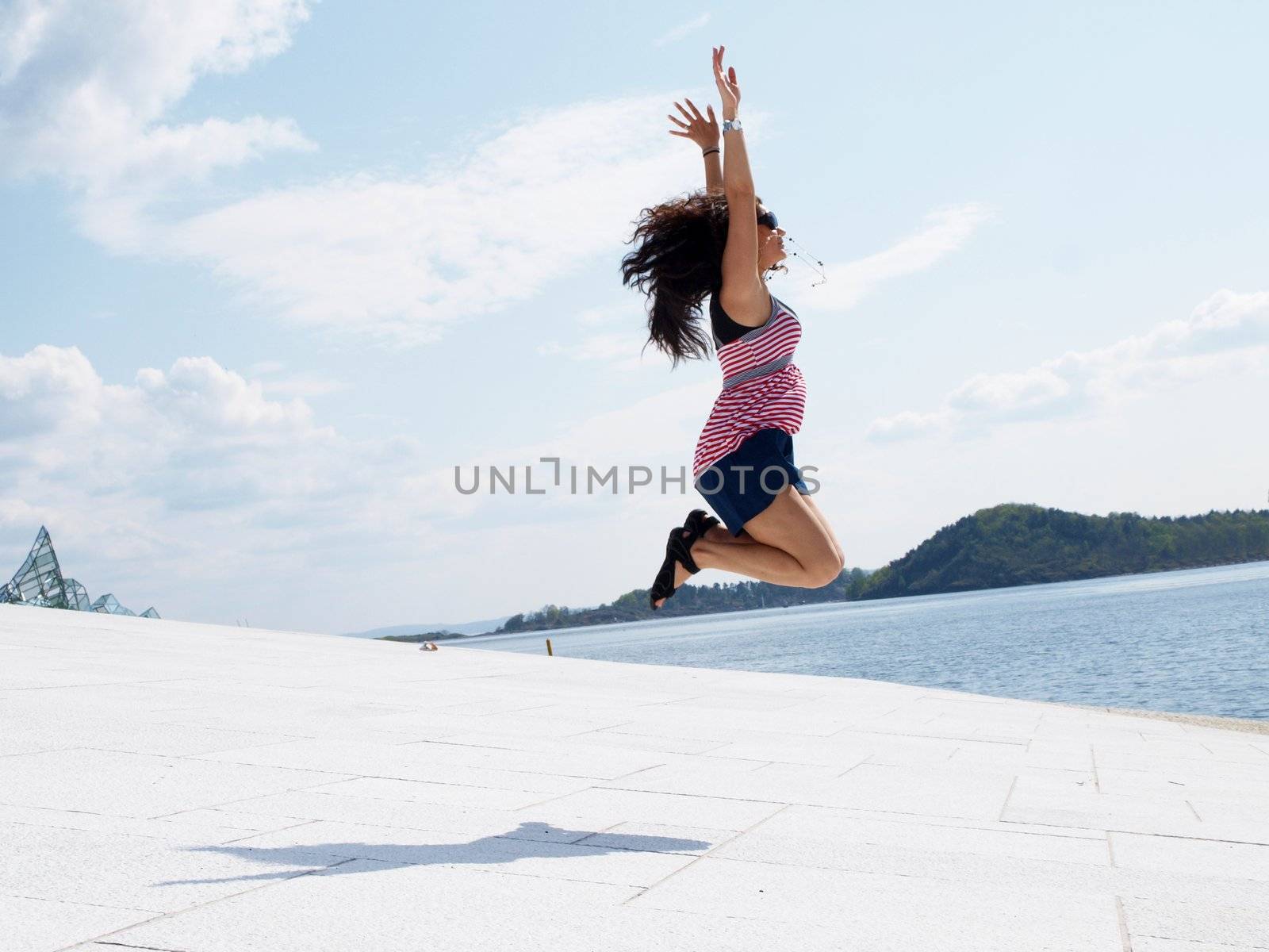 Young brunette female, jumping of joy on roof top by Arvebettum