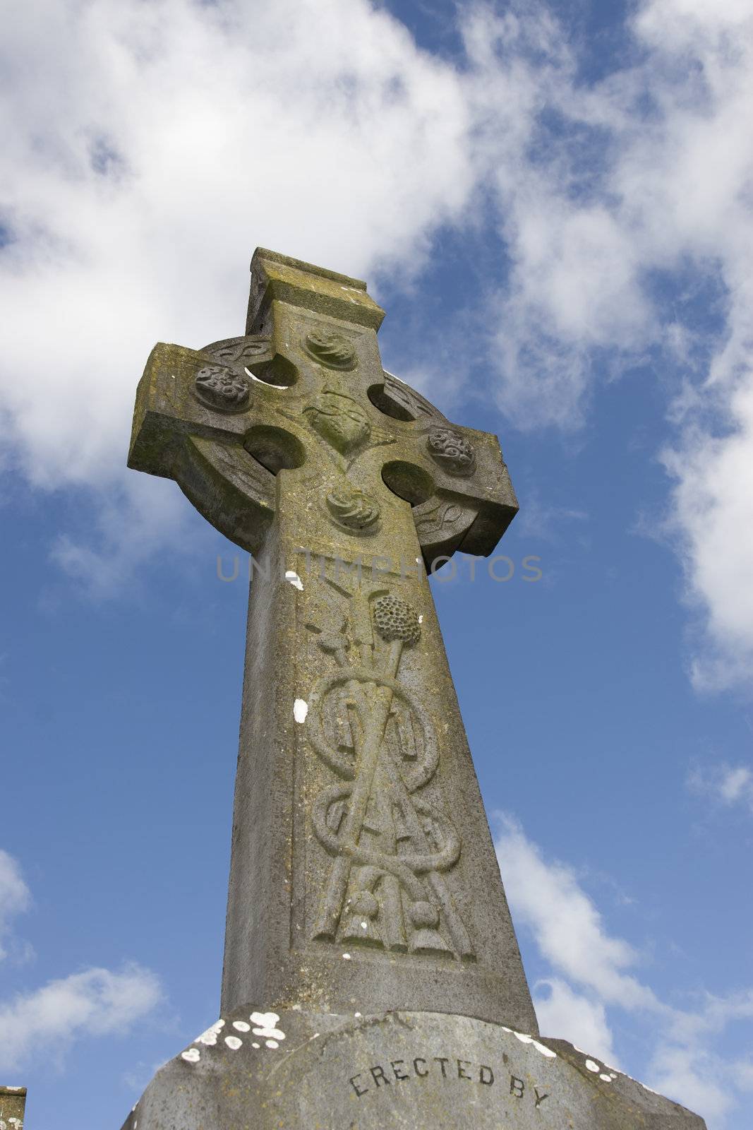 an old celtic cross in an irish graveyard with blue cloudy sky