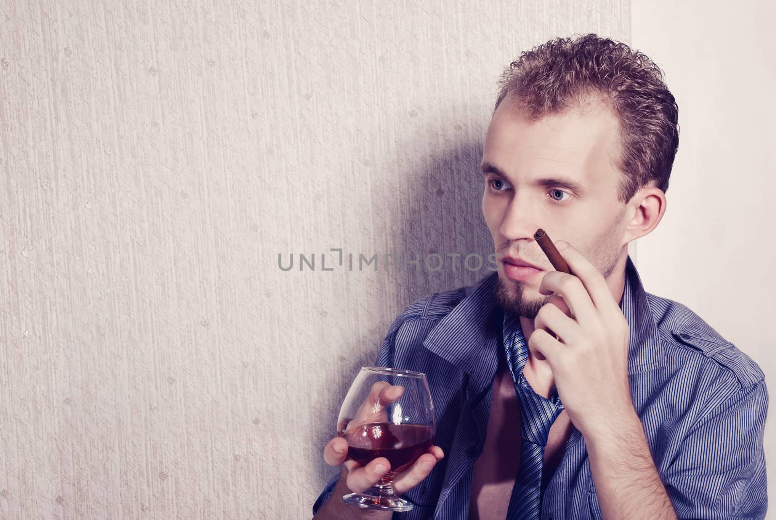 Elegant young handsome man drinking alcohol with a cigar in his hand. Fashion studio shot.