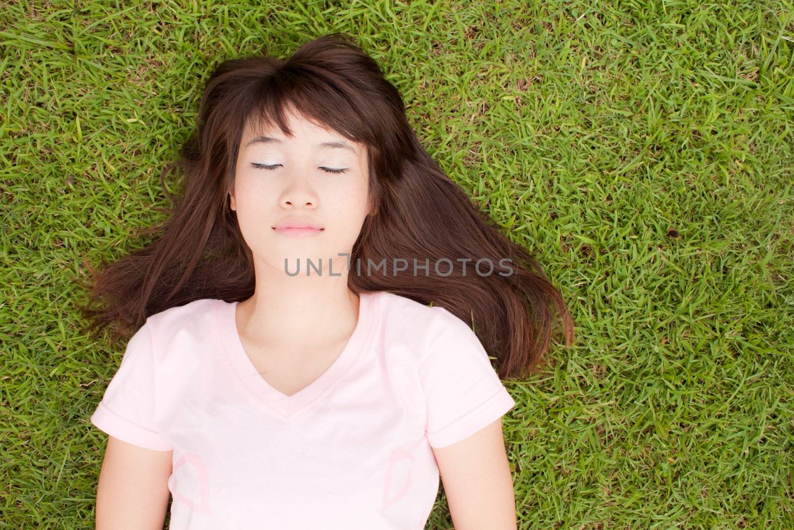 Beautiful Asian girl lying on the green grass field, enjoying with beautiful nature