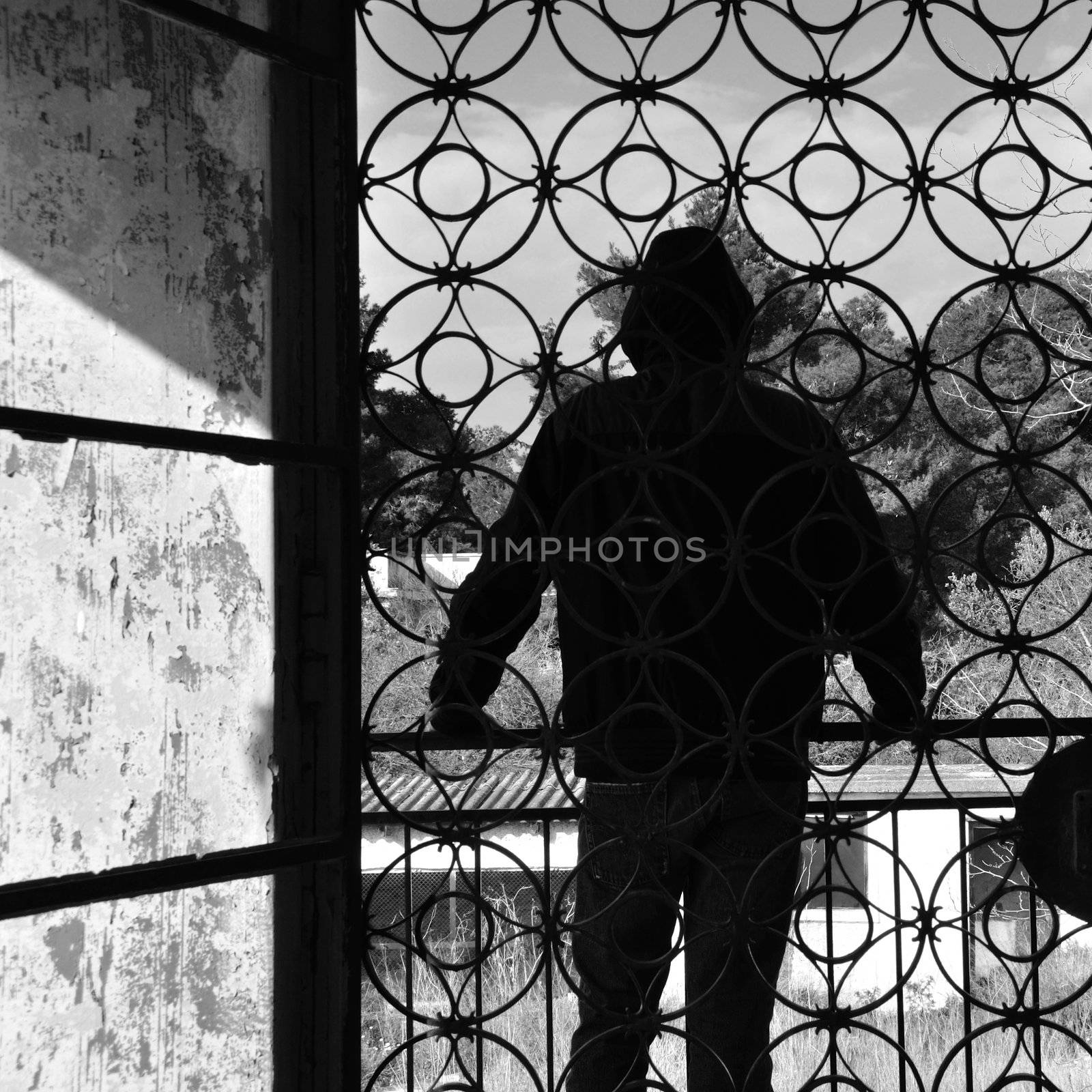 Man on the balcony of an abandoned house, metal door pattern. Black and white.