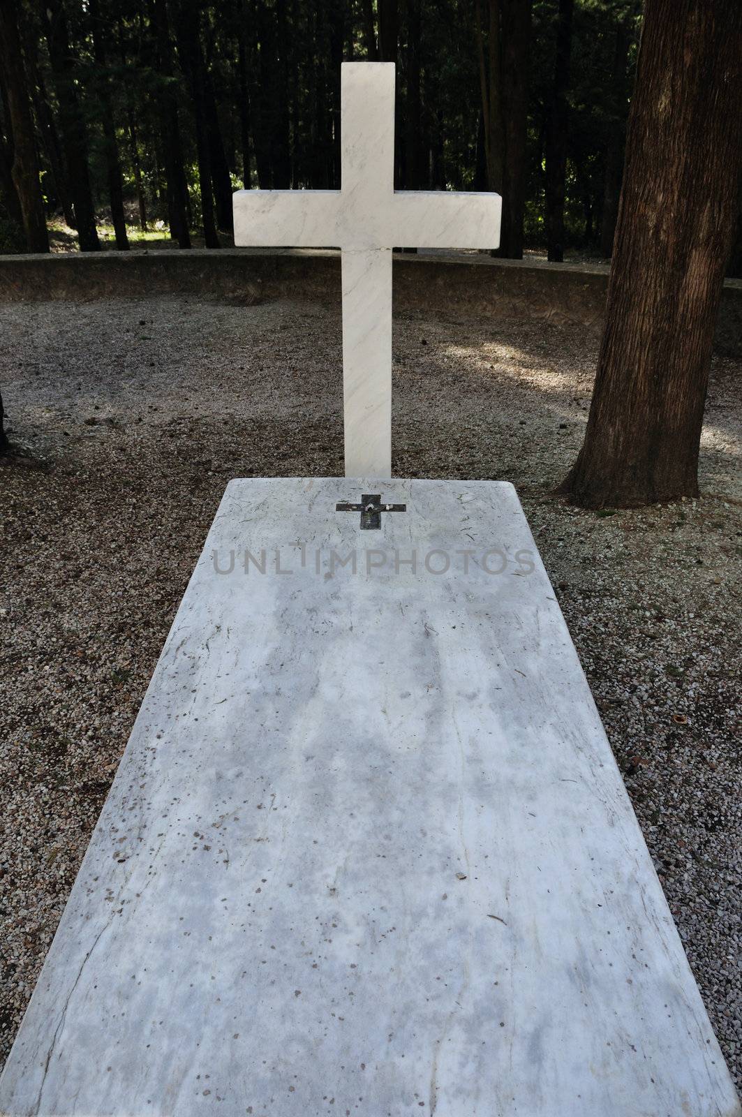 Cross and marble grave tombstone among trees.
