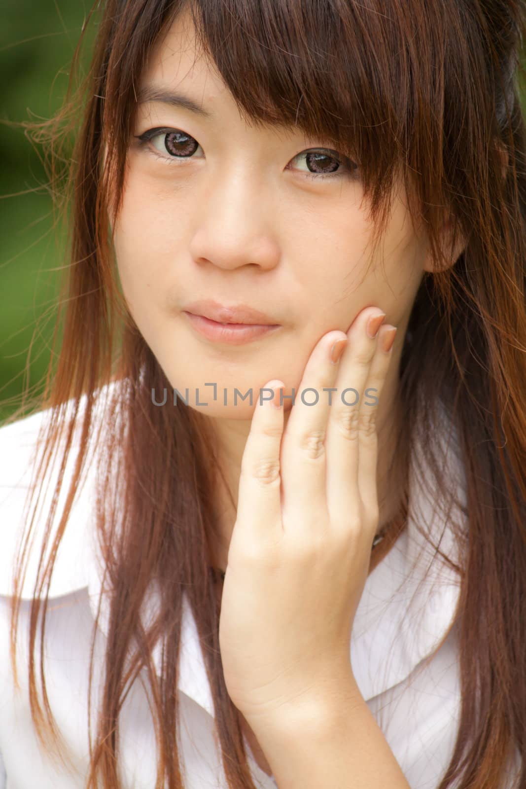 Heathy young Thai girl portrait in the green park, hand on her cheek