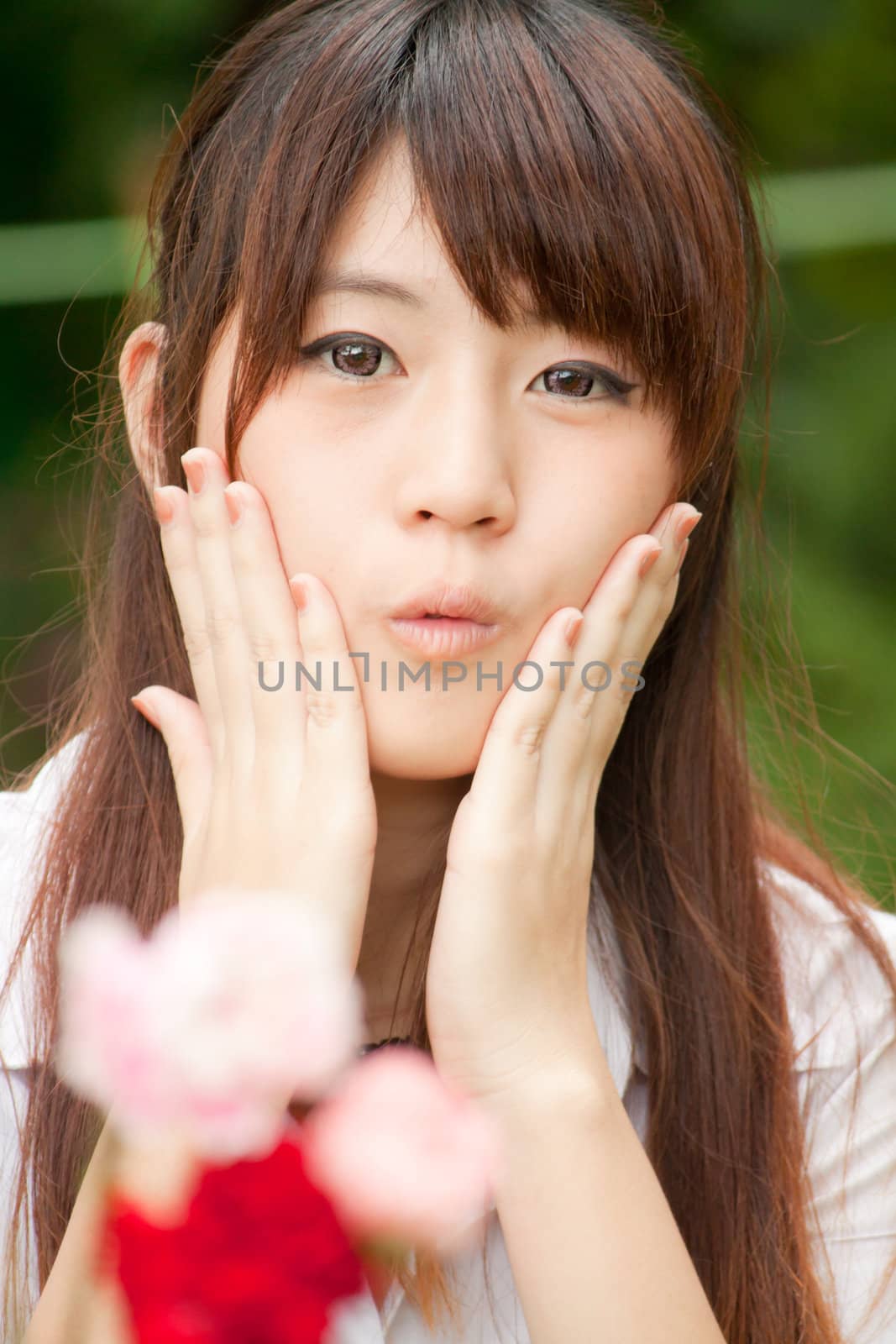 Young healthy Thai girl portrait in the park with flowers, focus at Model, hands on her cheek