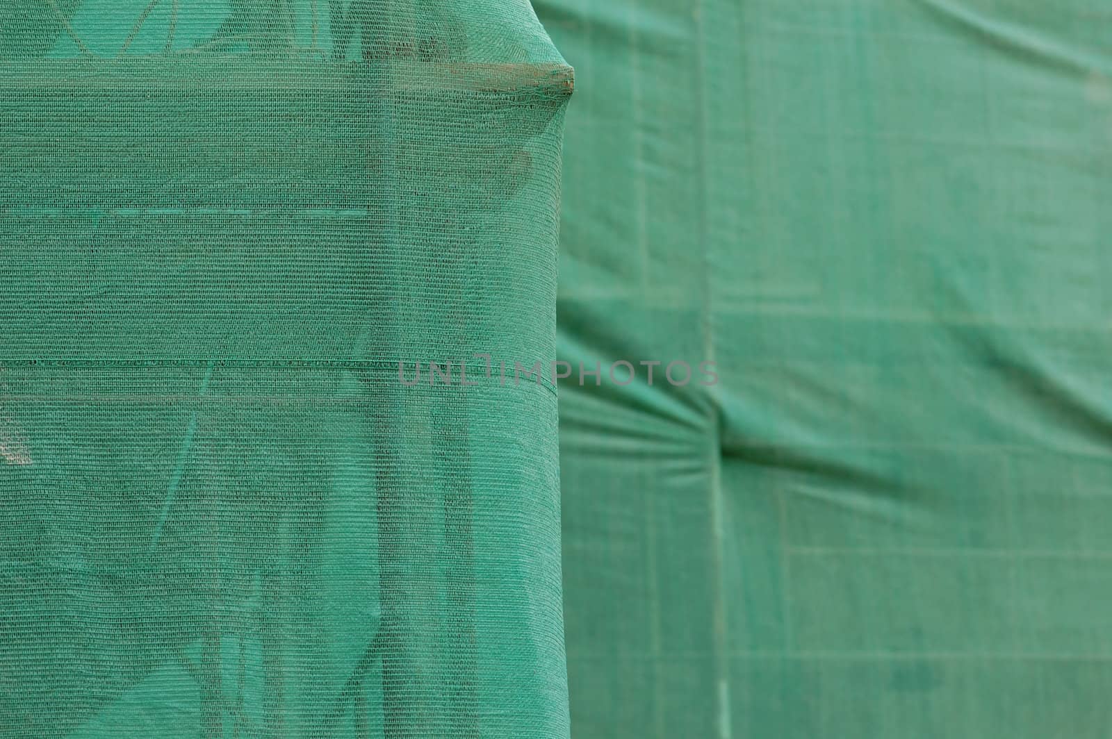 Scaffold under green debris netting at construction site. Abstract background.