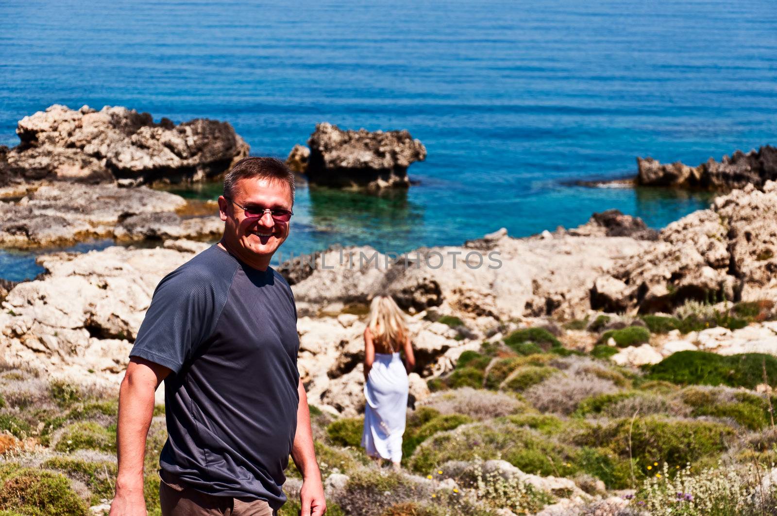 Smiling man and walking away blond in white dress on sea coast