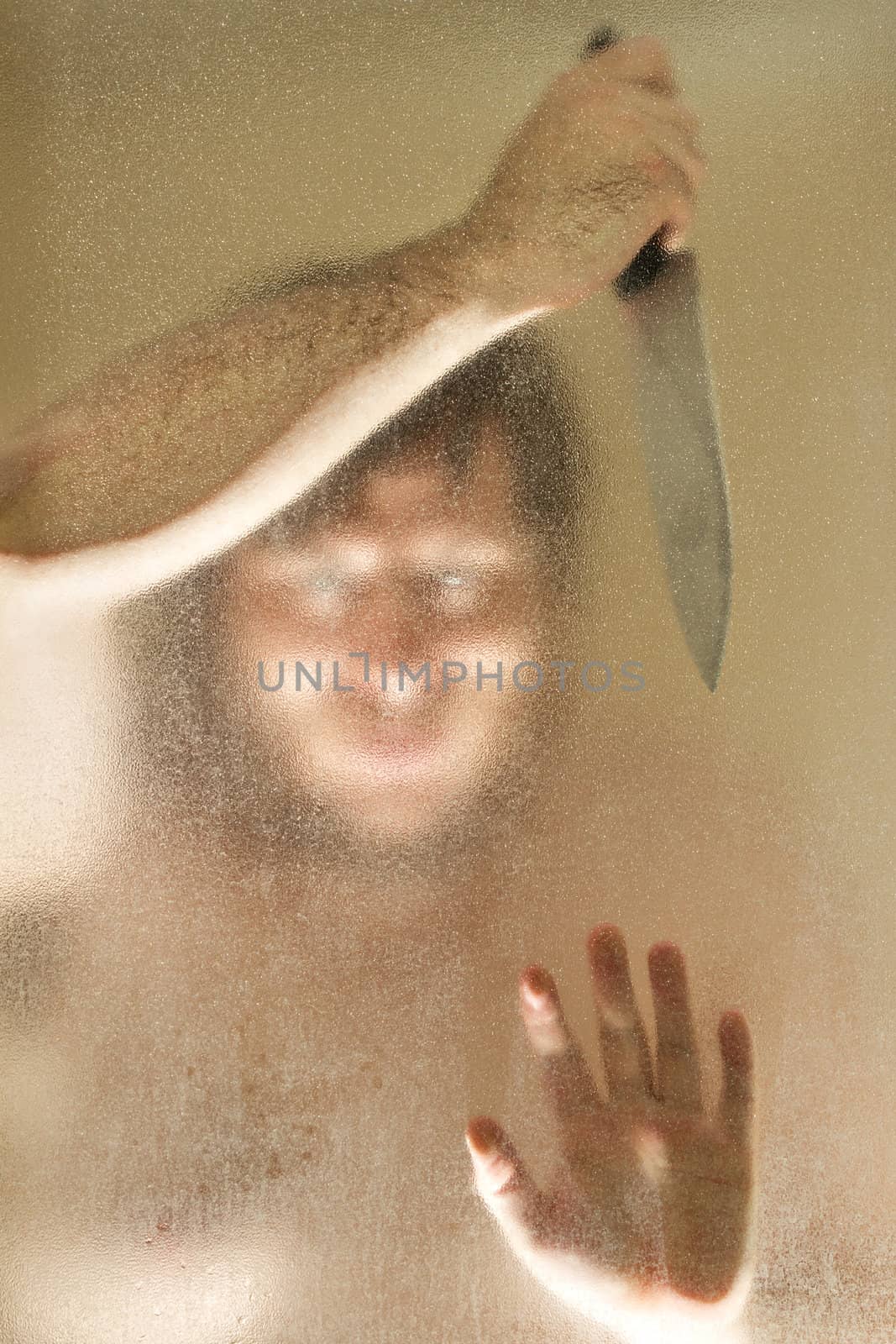 Man with a knife up against a shower door. Man's face is obscured mostly by the shower door