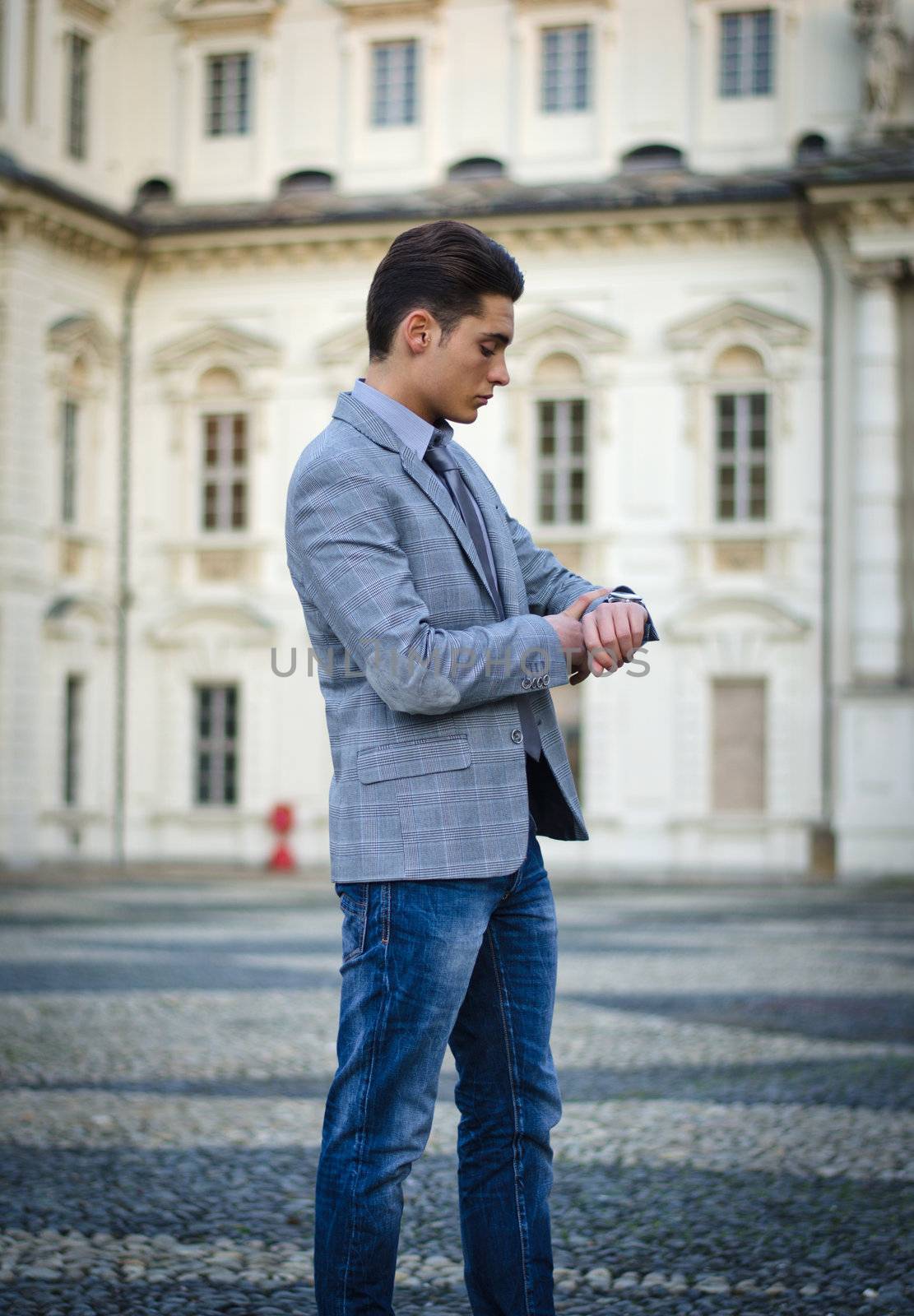 Attractive young man walking, elegant palace behind, checking the time